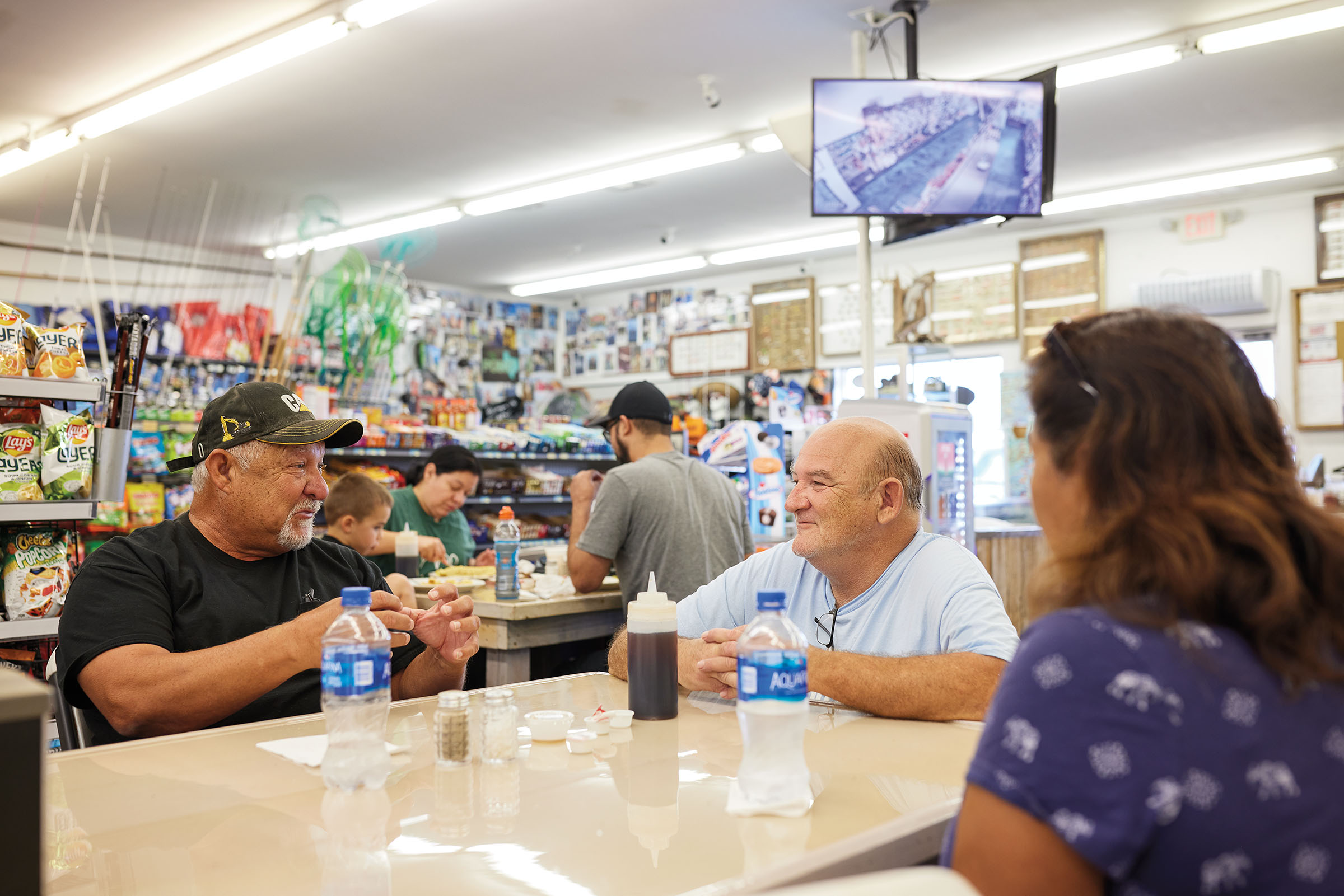 A group of people sit talking at a table inside of a busy conveinence store