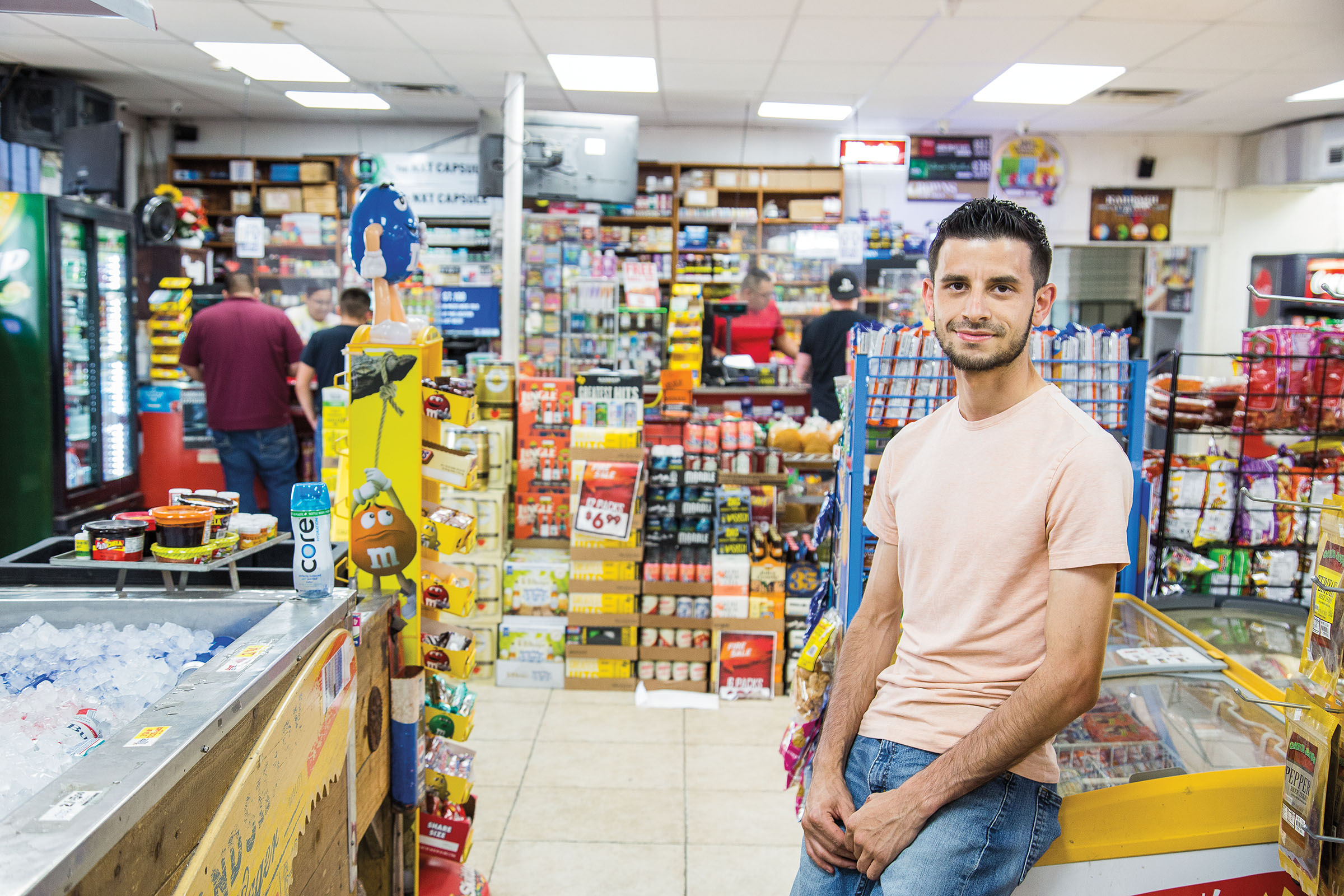 A man in a t-shirt leans against the counter of a store
