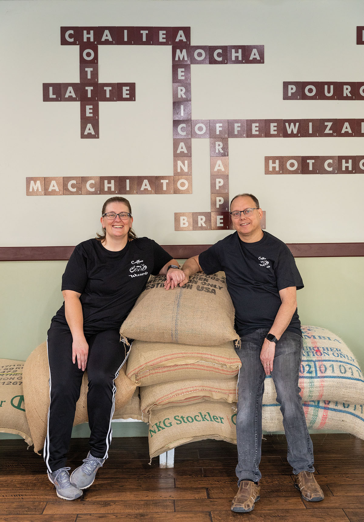 Two people sit on a large stack of coffee beans in burlap sacks