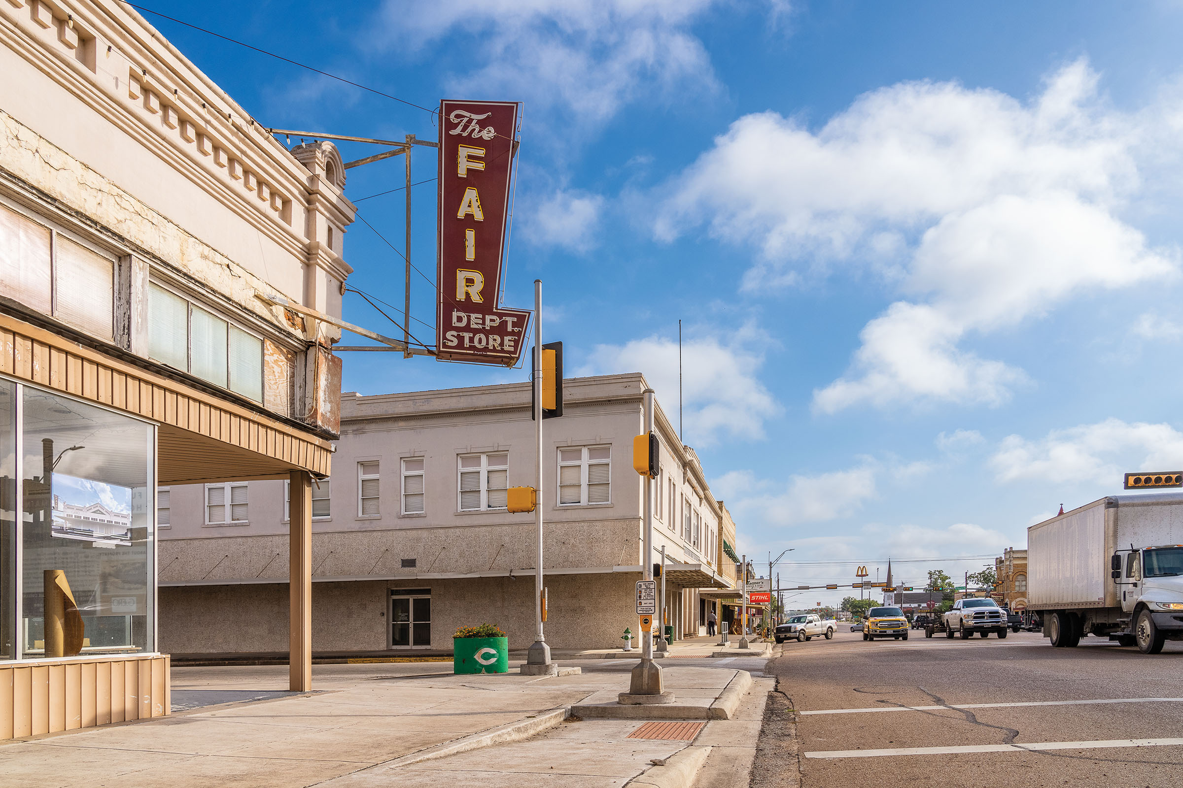 A downtown scene with a red sign reading "Fair Department Store" under blue sky