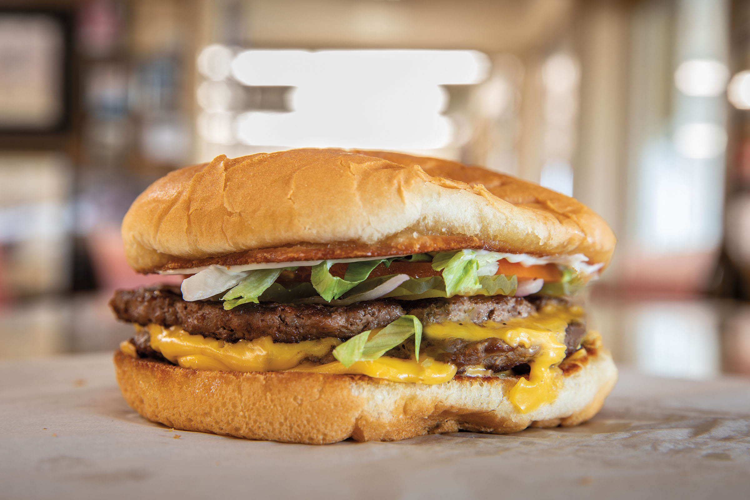 A side view of a cheesburger with lettuce and tomato on a golden brown bun