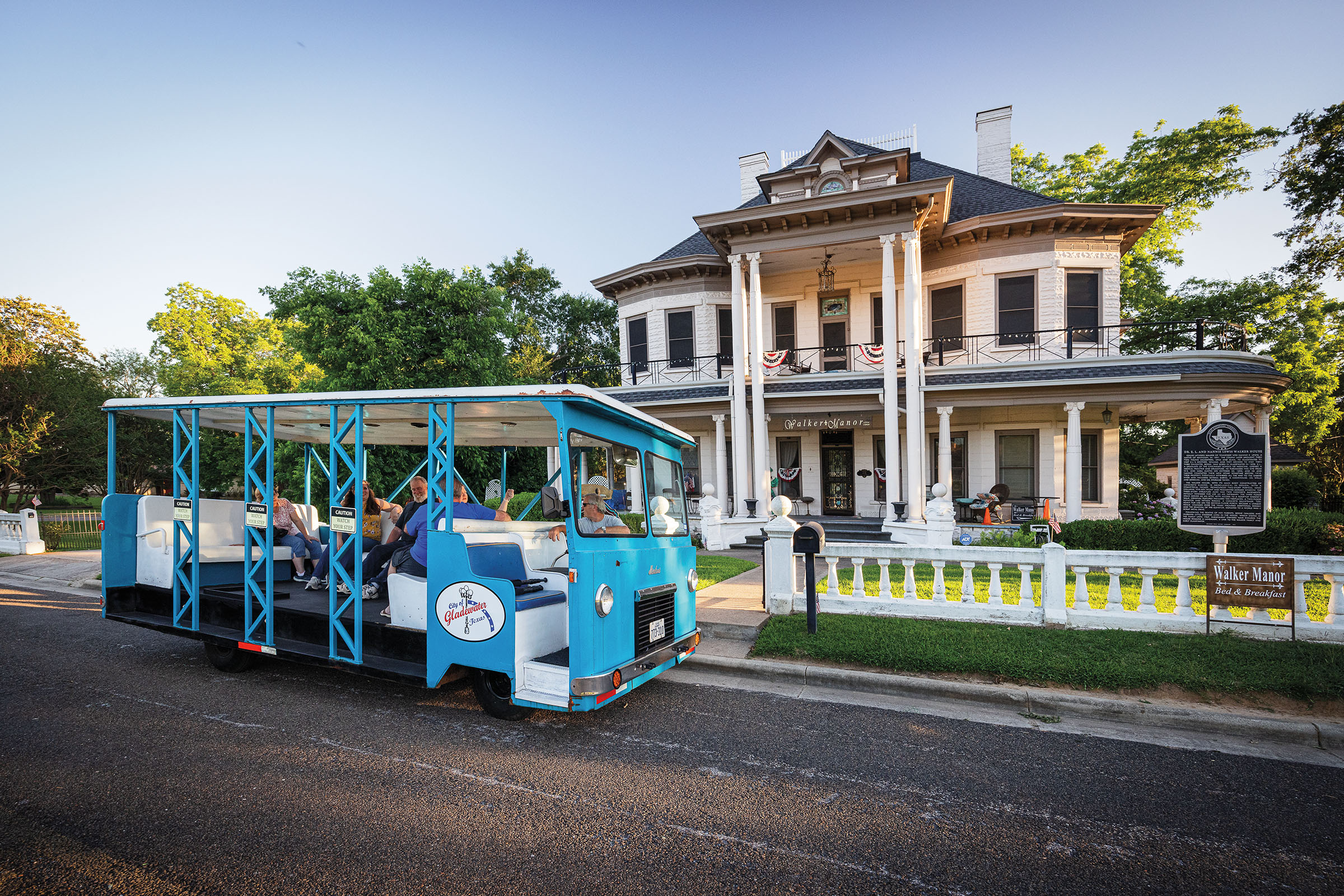 A bright blue trolley out front of an historic home