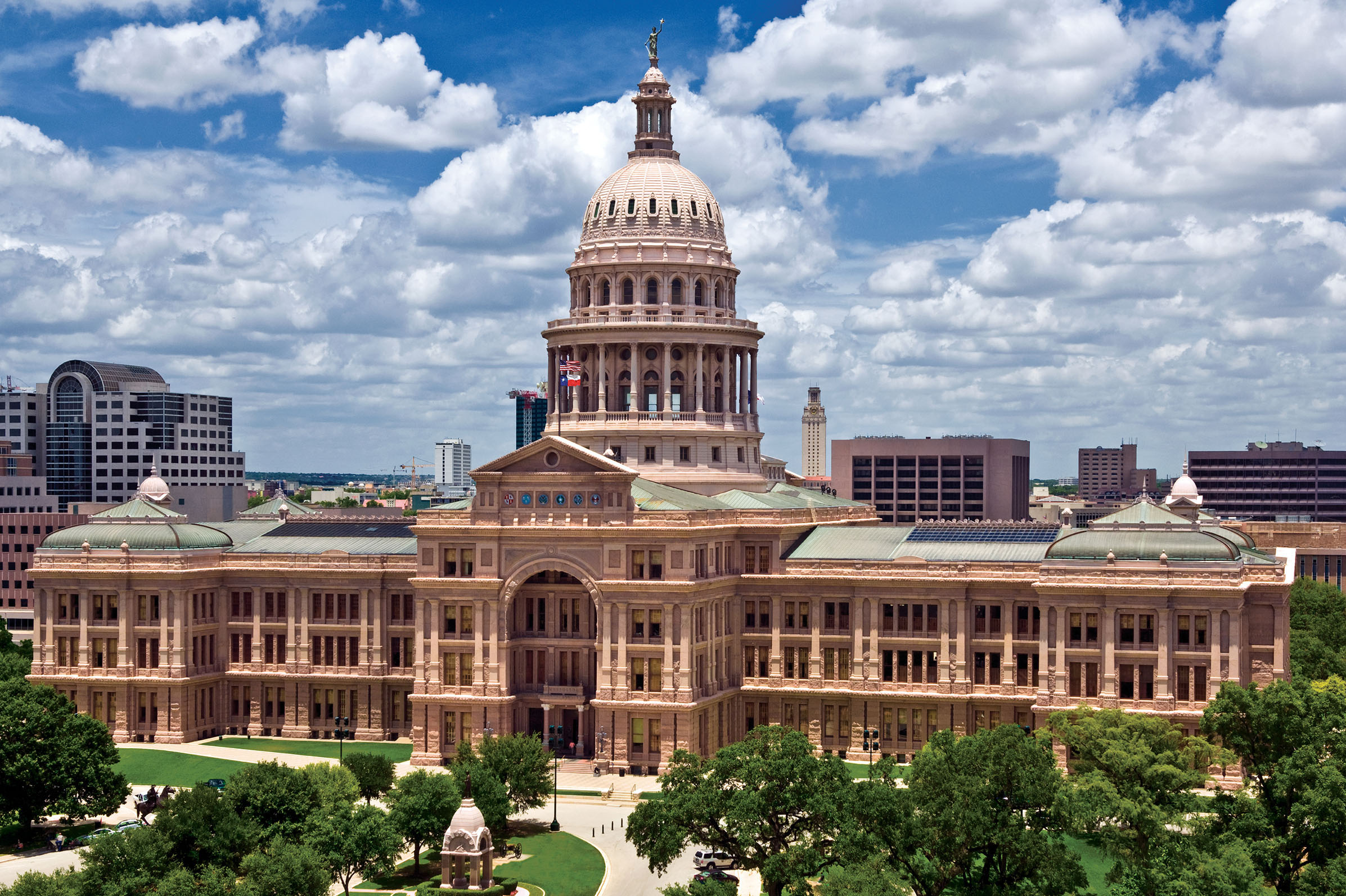 The pink Texas State Capitol stands tall under a bright blue sky dotted with clouds