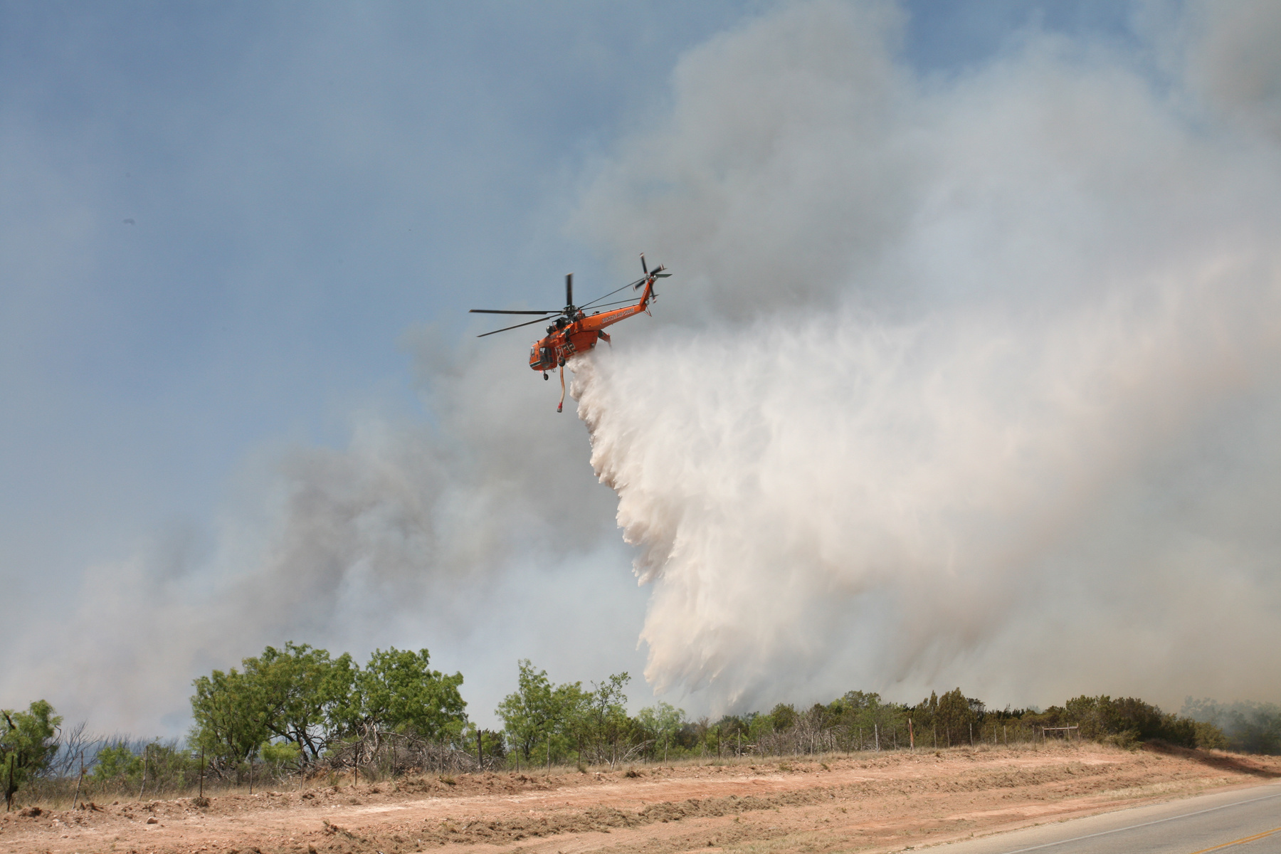 Red helicopter dropping down water onto a wildfire in Tom Green County