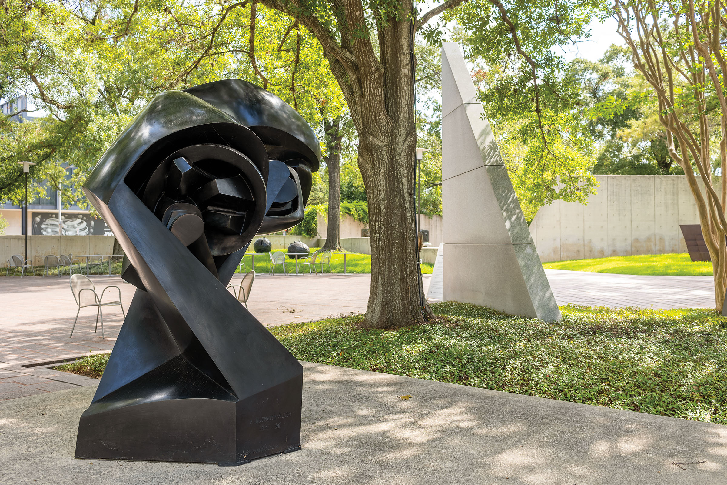 An abstract sculpture made of black material on a concrete slab surrounded by green trees