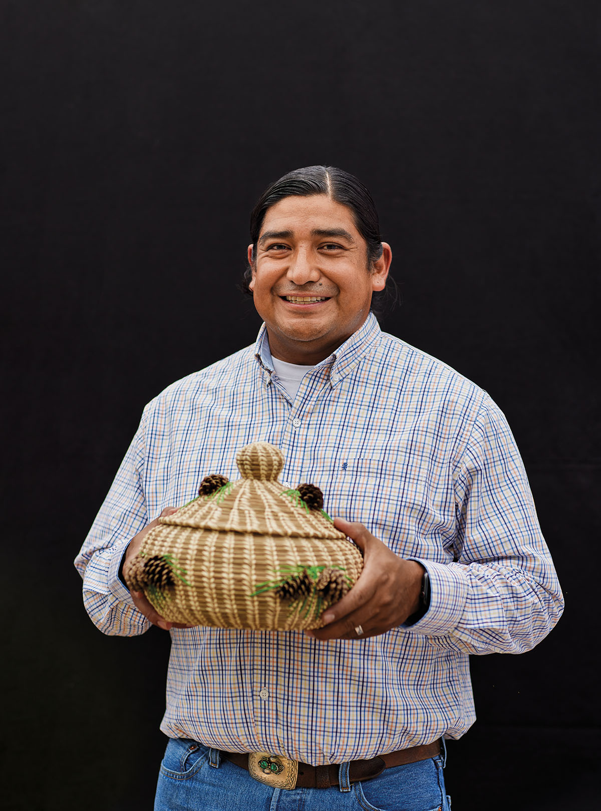 A man in a collared shirt holds a small woven basket in front of a dark background