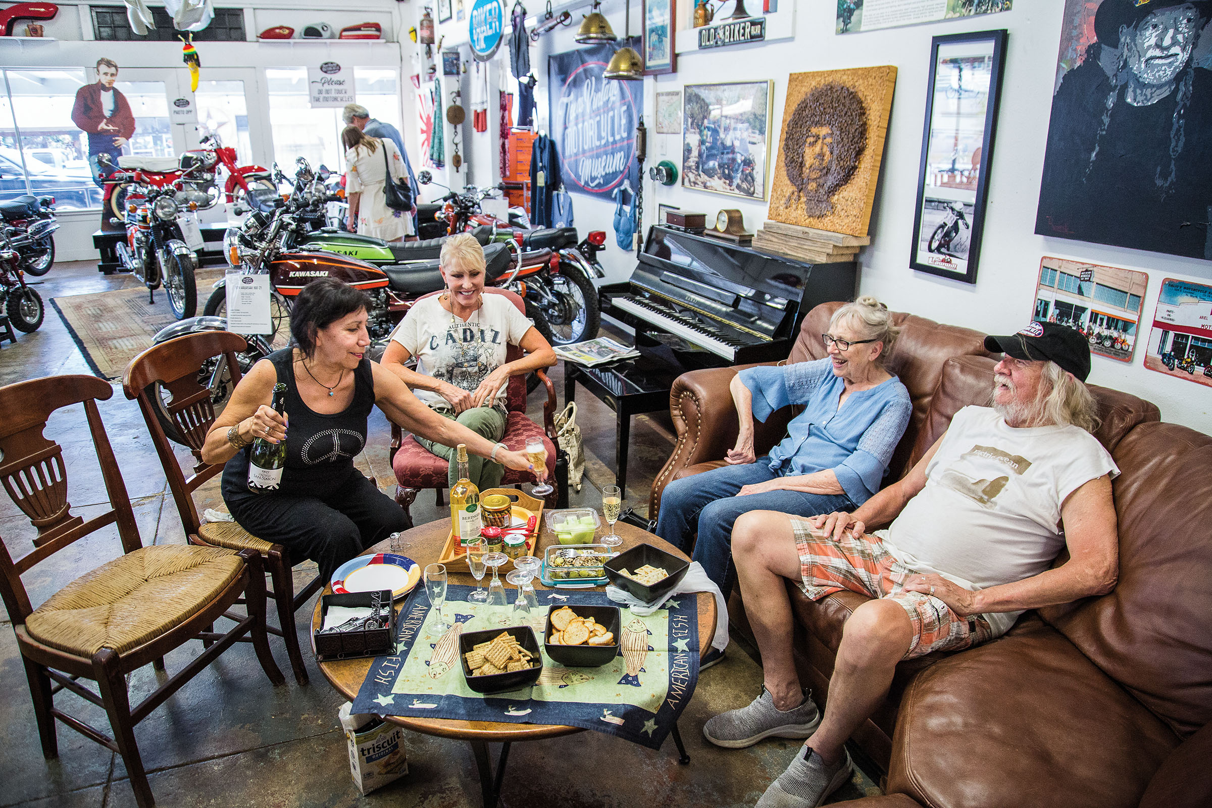 A group of people sit in leather chairs with bottles of wine and plates of crackers