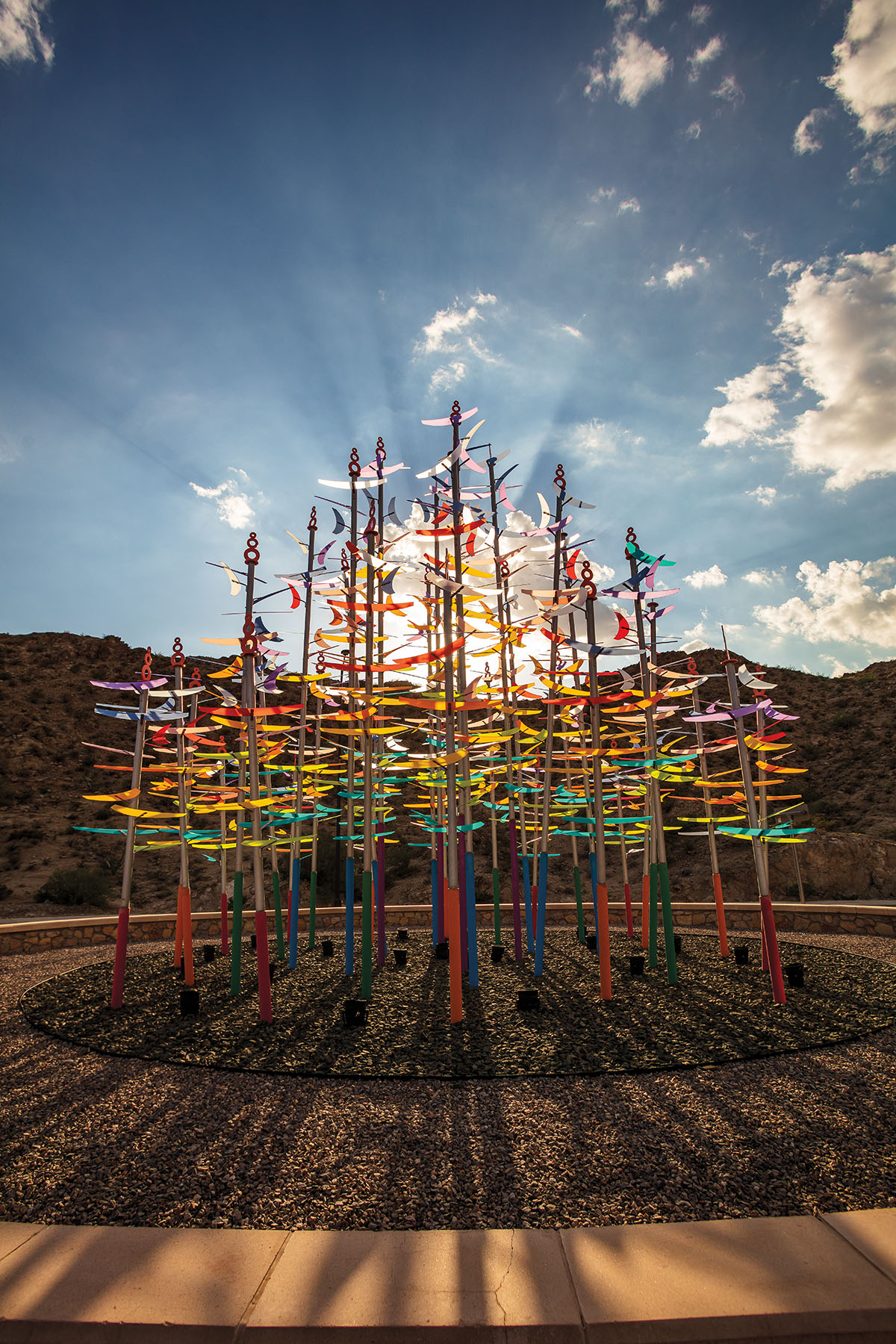 Brightly colored spires illuminate a landscape in front of blue sky with streams of light and white clouds