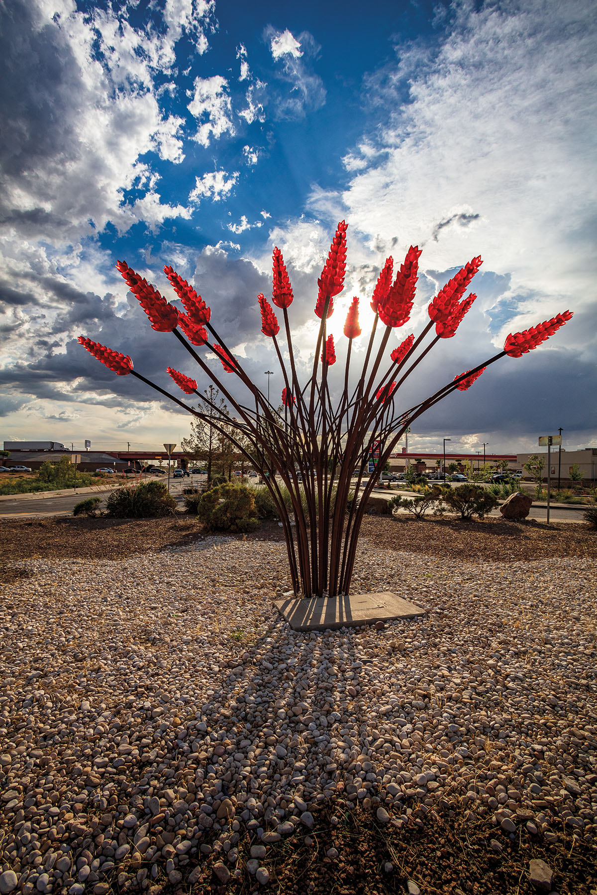 Bright red metal and glass form the shape of an ocotillo plant in a rocky landscape under blue sky
