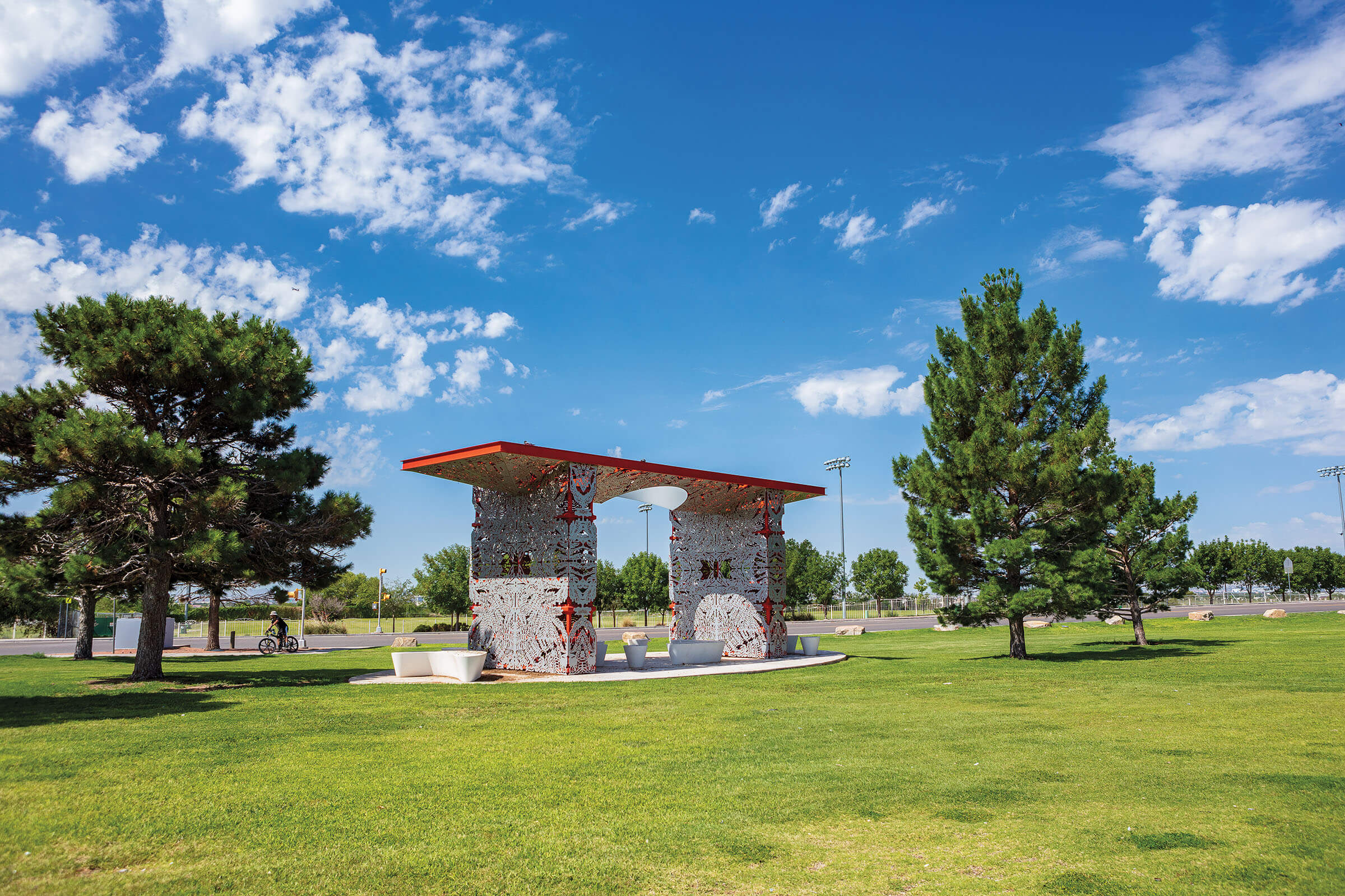 A stone pavillion with a red roof on green grass under bright blue sky