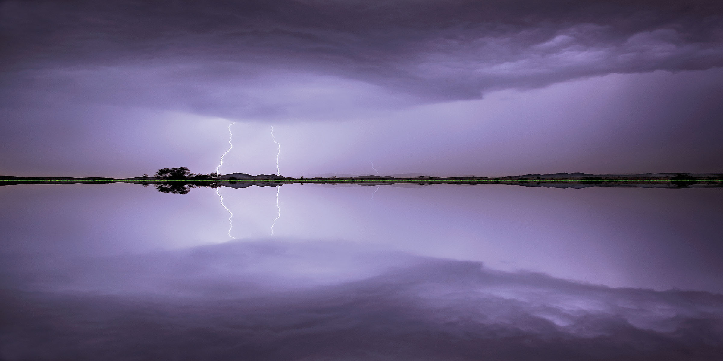 A reflection of a lightning storm on a large body of water with purple sky