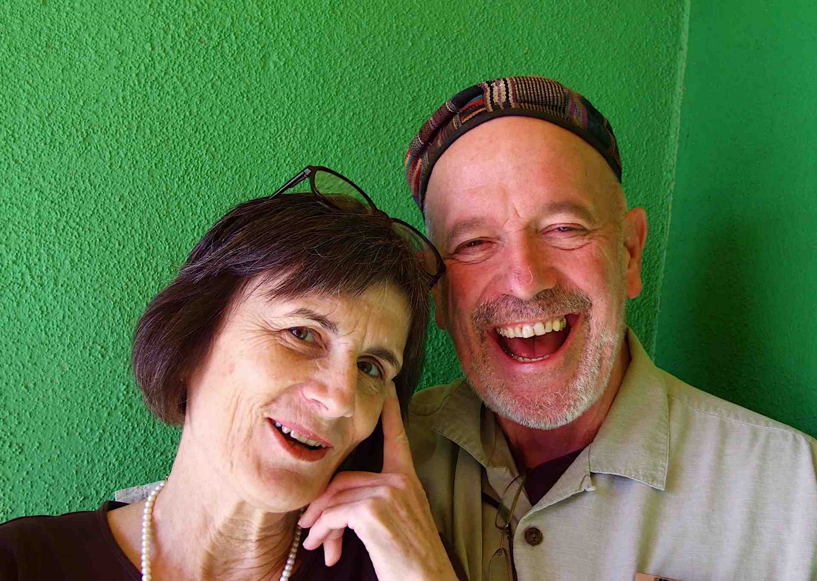 woman with glasses and man with hat in front of green wall