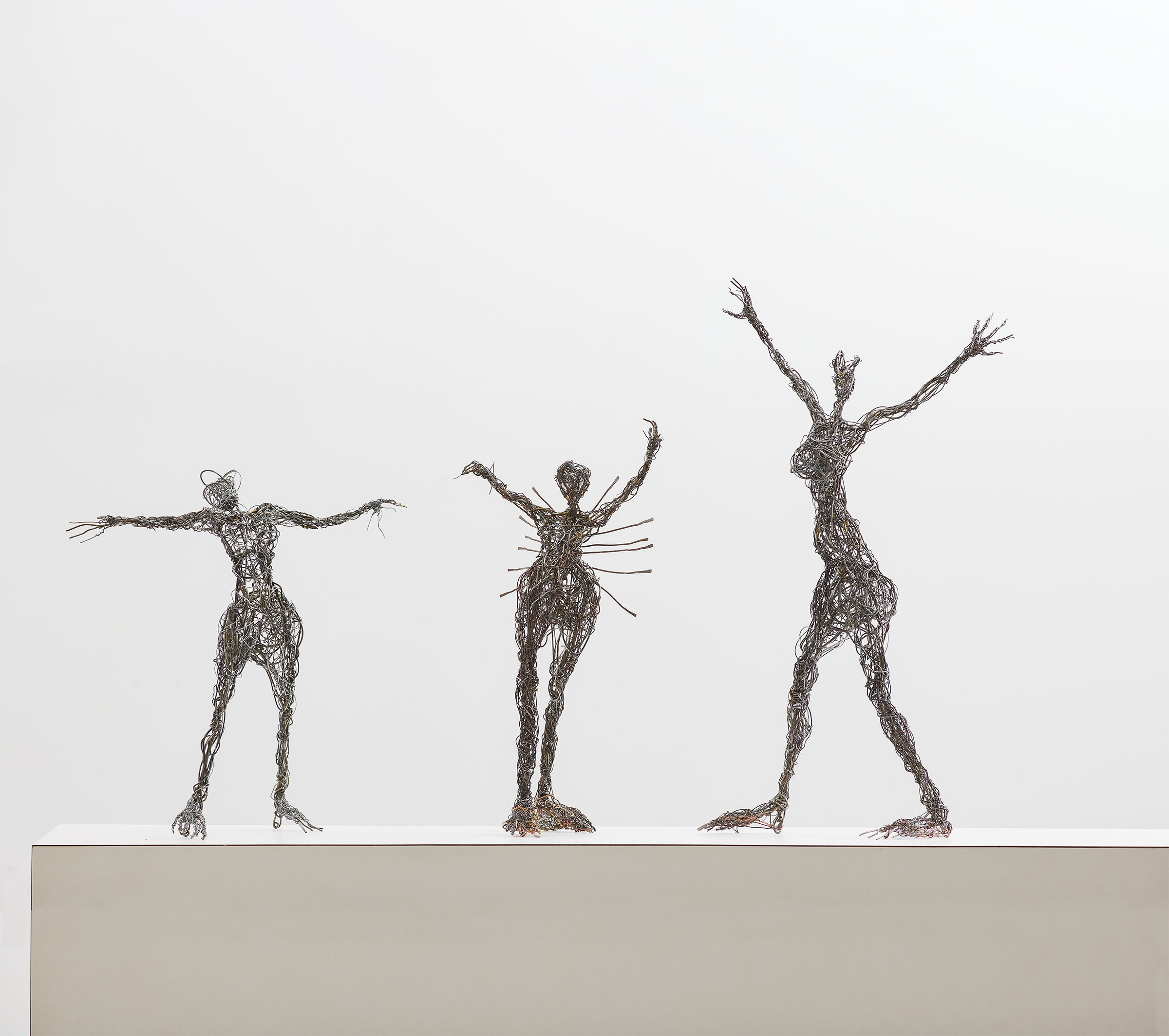 Three thin sculptures on a tan horizon line in front of a light gray background