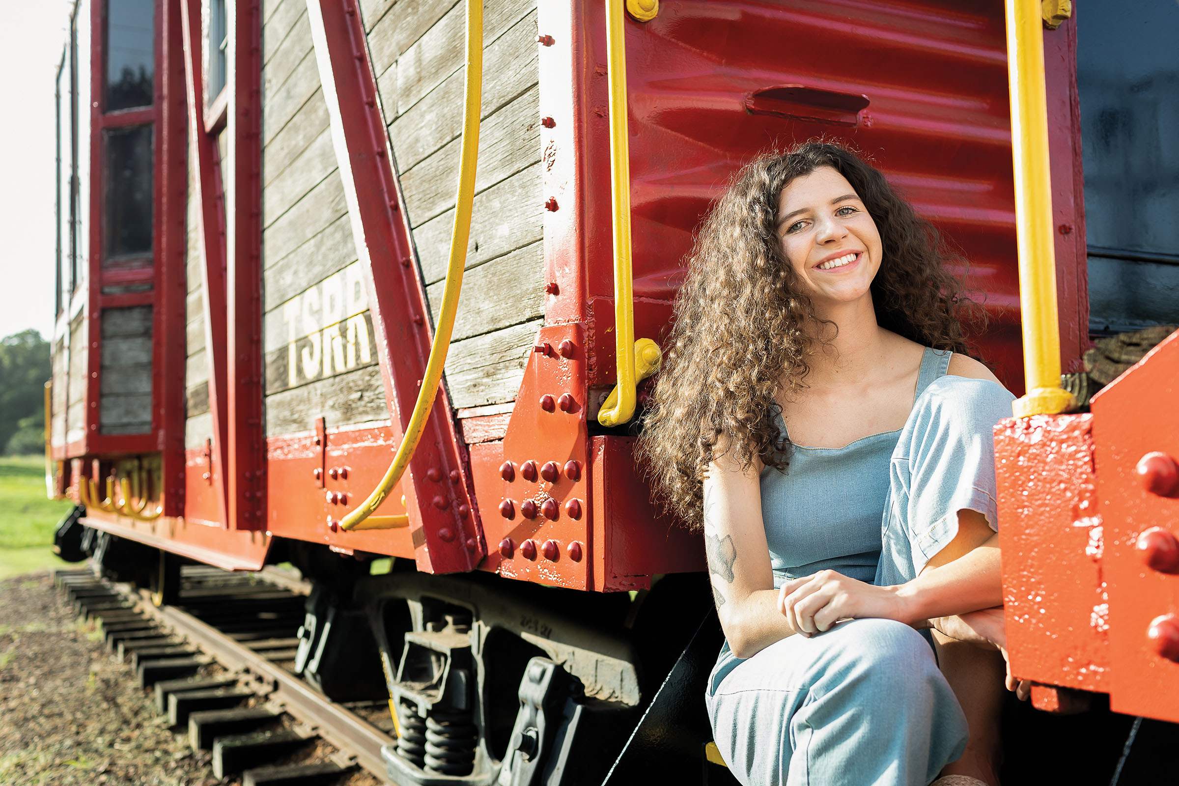 A woman sits on the side of a red and wood boxcar