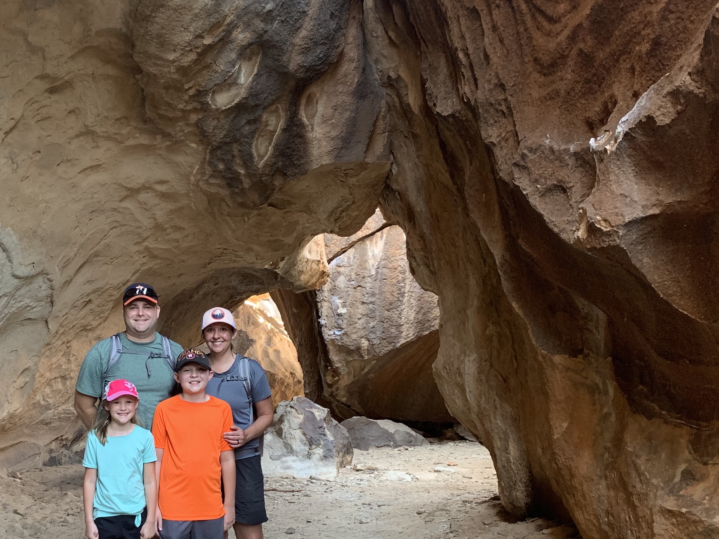 Two parents and their young children in front of an impressive rock formation that looks like a cavern