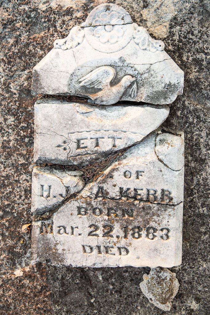 A broken white concrete headstone with slightly readable text, indicating the person died Mar. 22, 1883