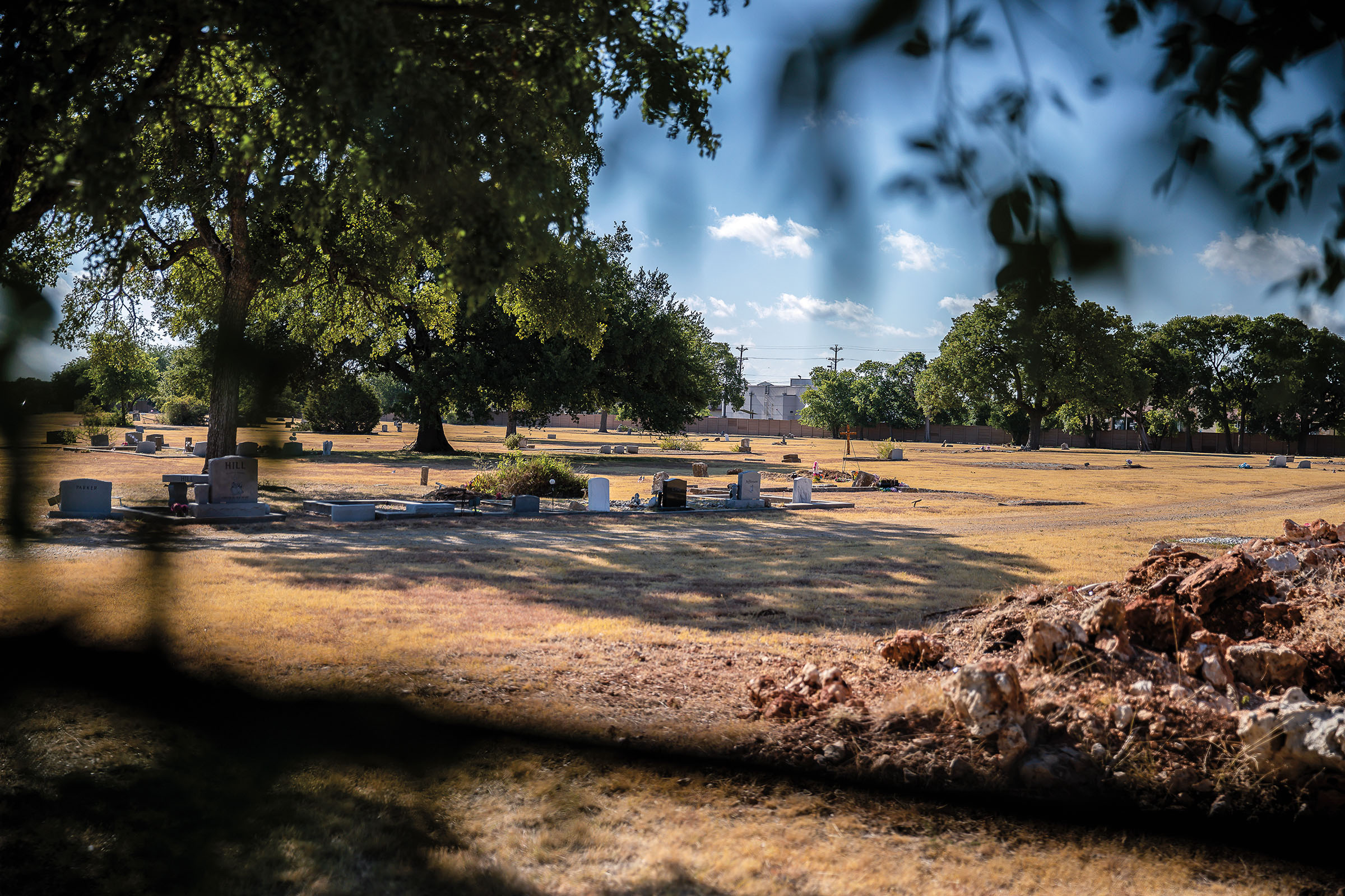 A view of a collection of headstones on a tan grassy field under blue sky