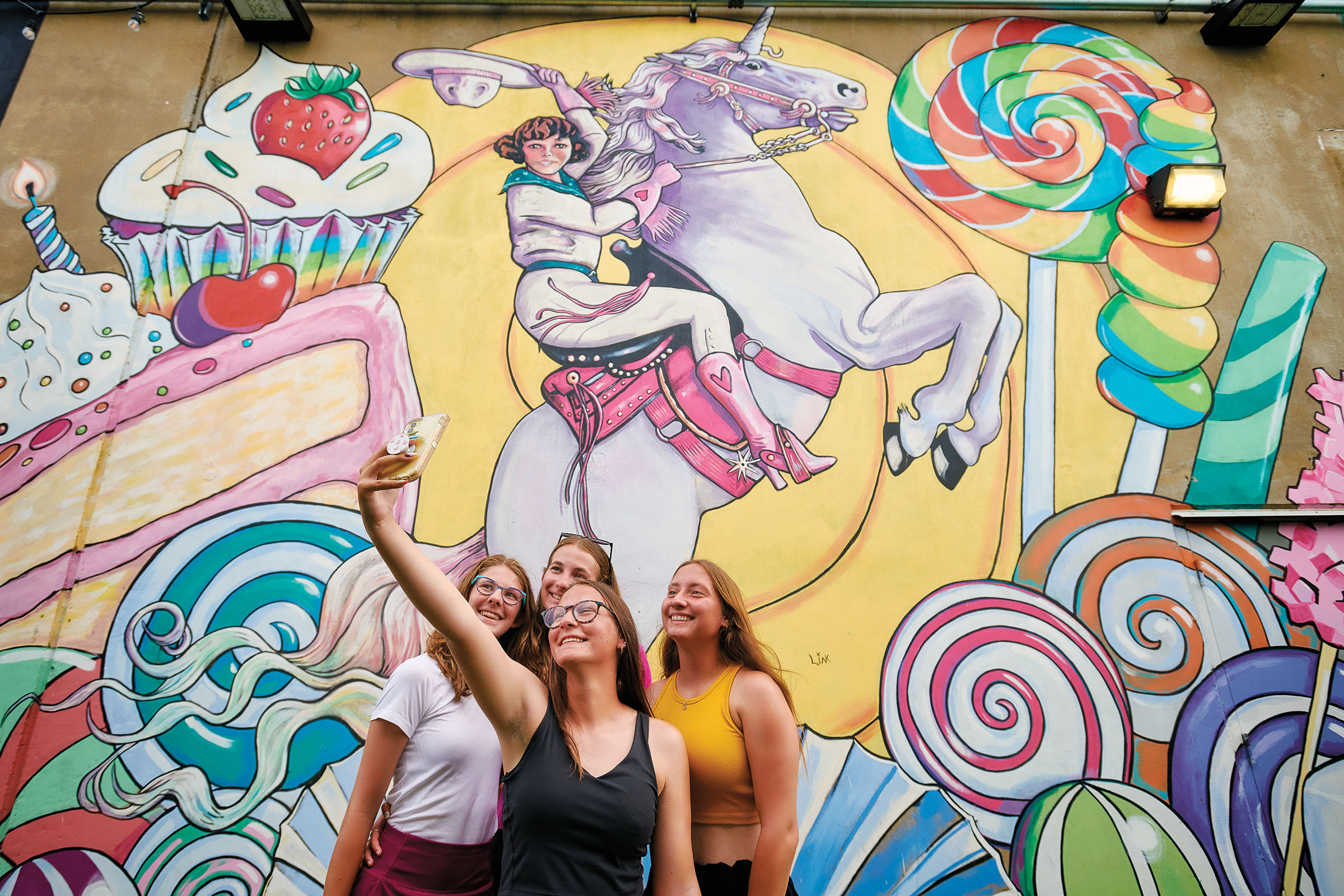 A group of people pose for a selfie in front of a brighty colored mural