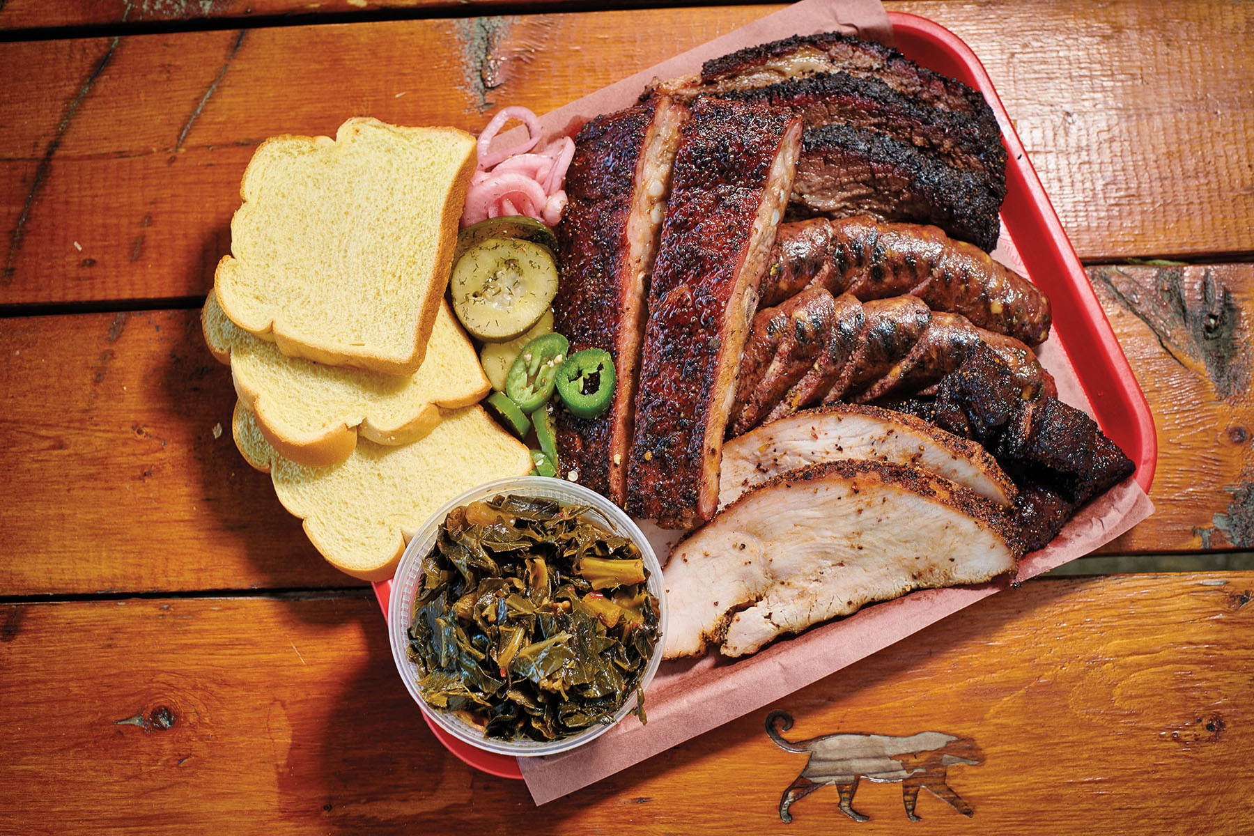 A platter of barbecue including brisket, sausage, turkey, ribs, white bread, and collard greens