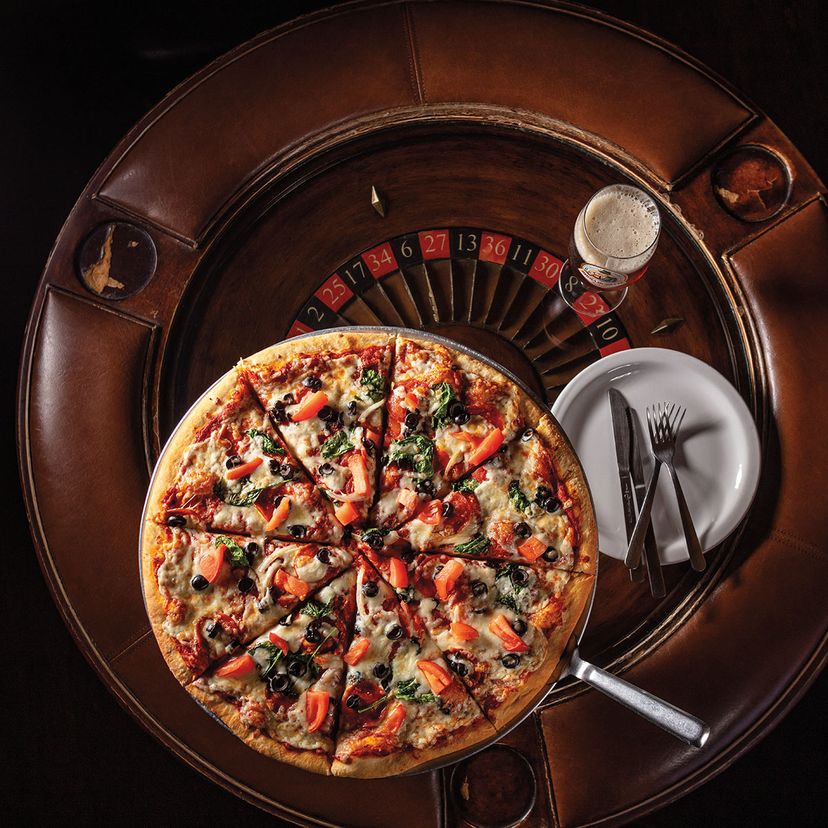 An overhead view of a pizza with tomatoes, spinach and other toppings on top of a roulette board