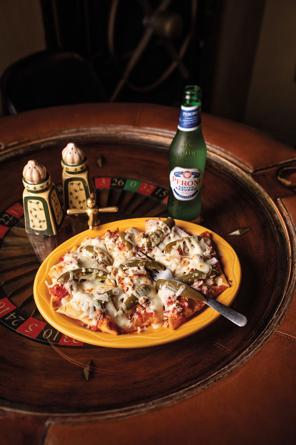 A yellow platter with large pieces of pasta, cheese, and a fork next to a Peroni beer