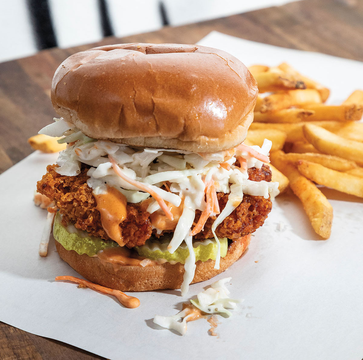 A vegan chicken sandwich topped with coleslaw on a Brioche bun served with a pile of golden French fries