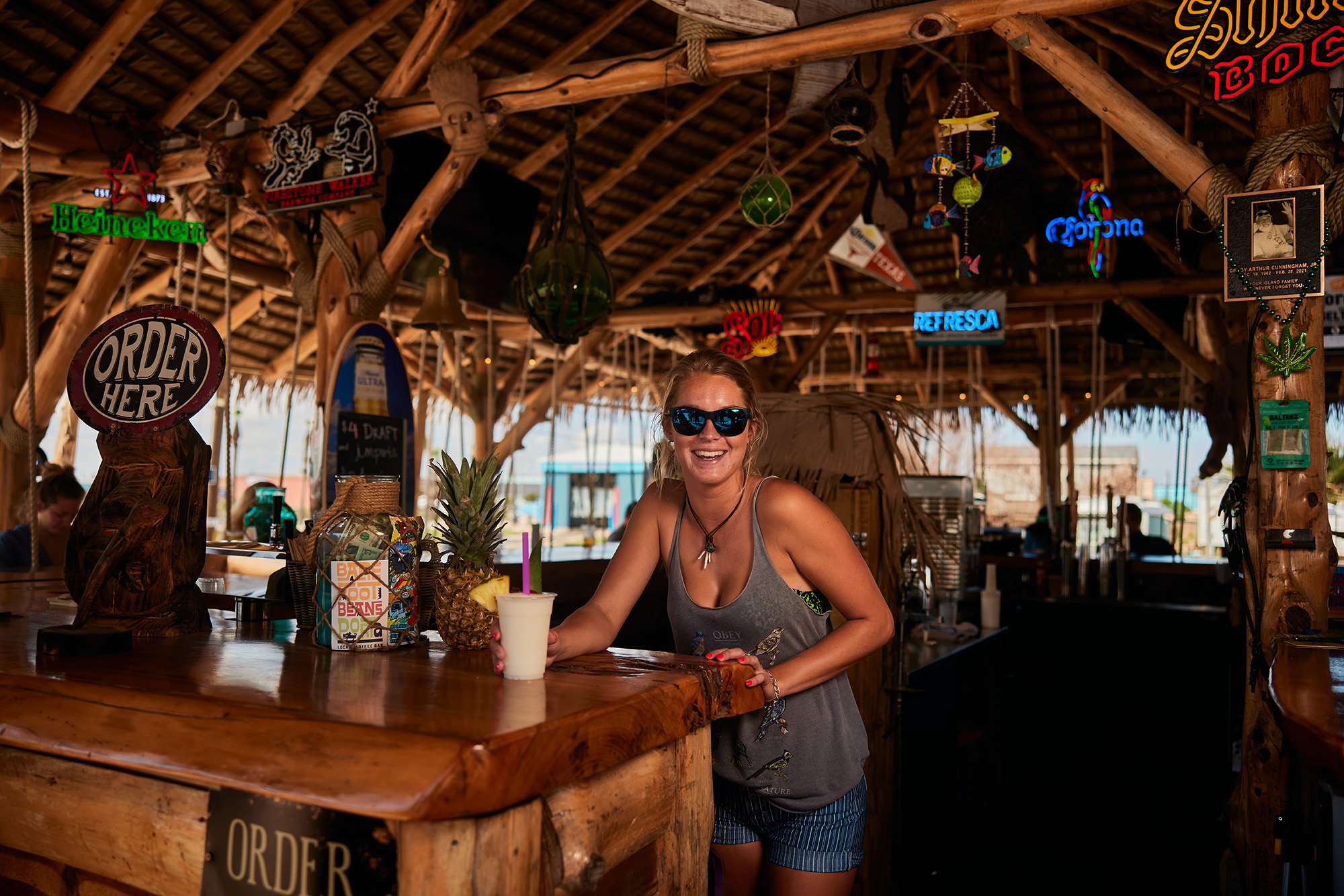 A woman stands at a table in the wood-paneled interior of Port Aransas' Beer Hut with a drink