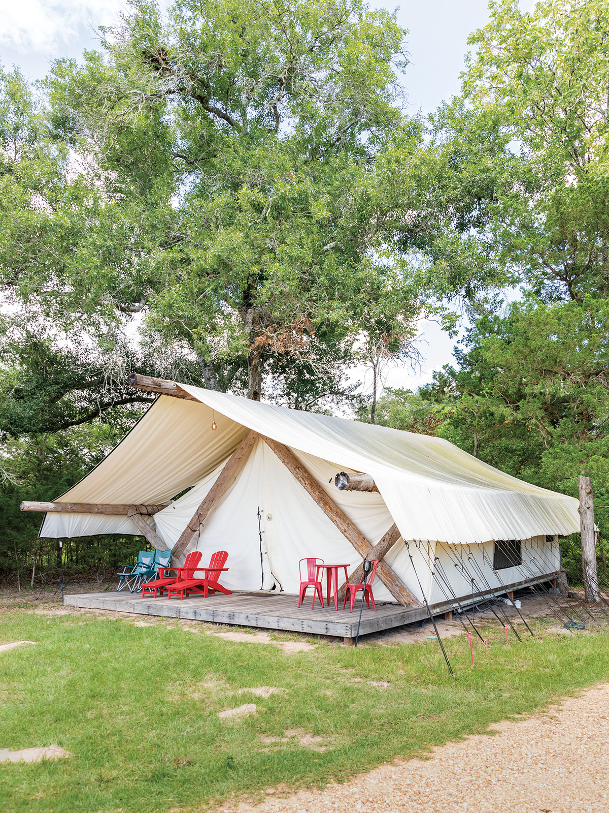 The exterior of a white tent with lawn chairs on the front in a green area