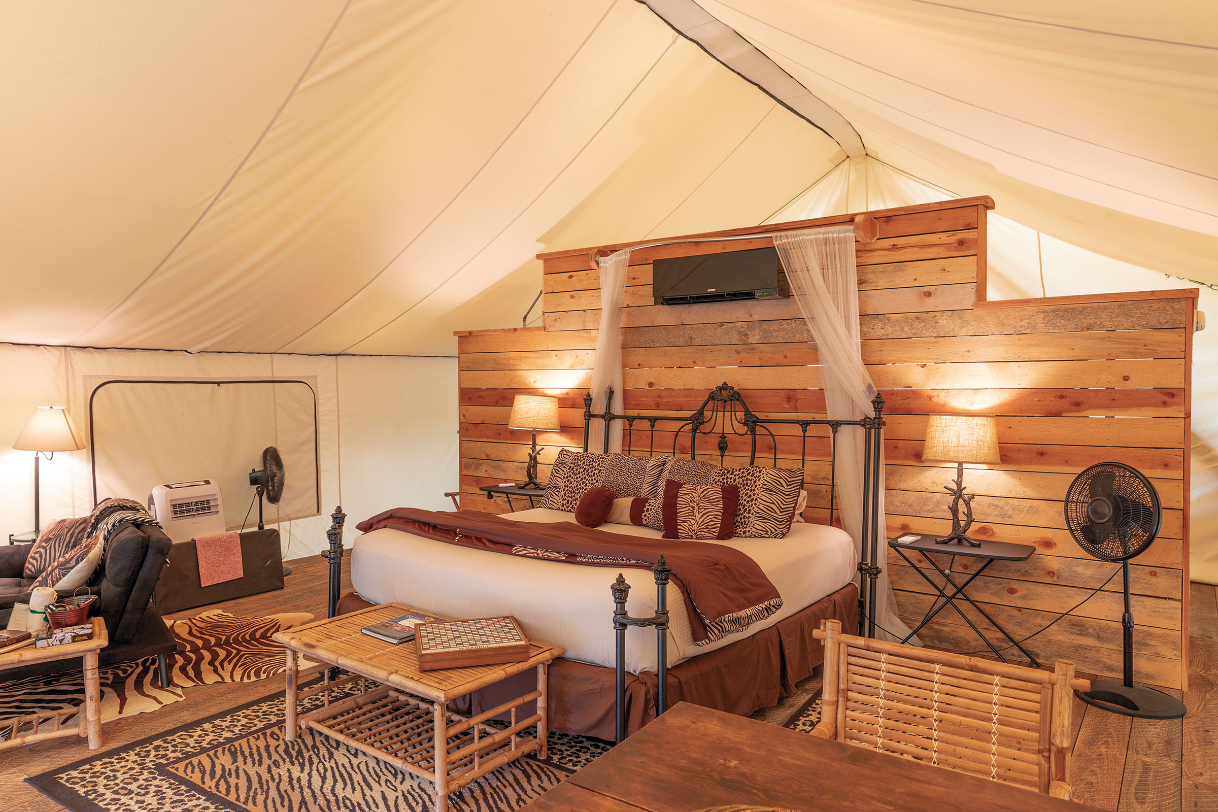 A view of a richly decorated interior of the Grand Safari Tent, including a large bed, wood paneling, and white canopy roof