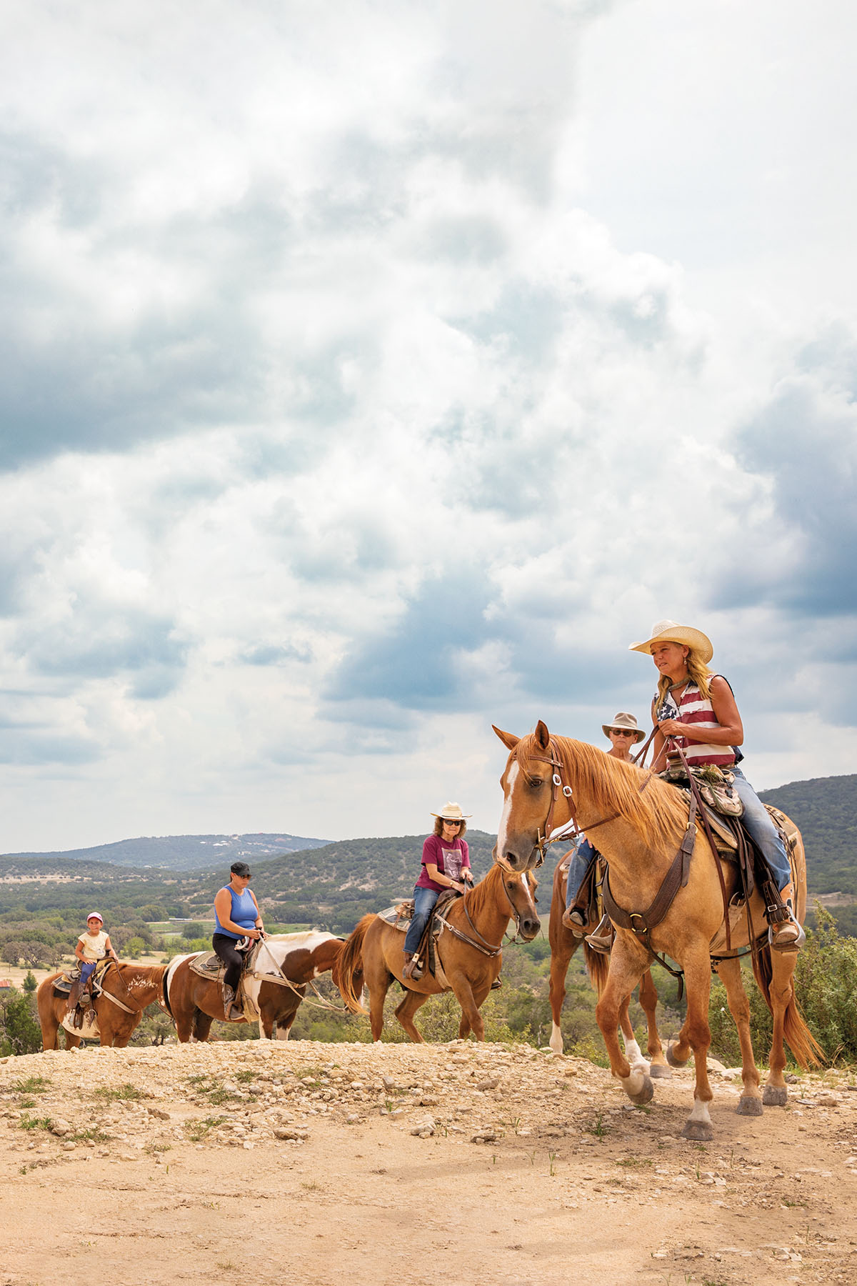 A group of people ride horses on a dusty trail under cloudy sky