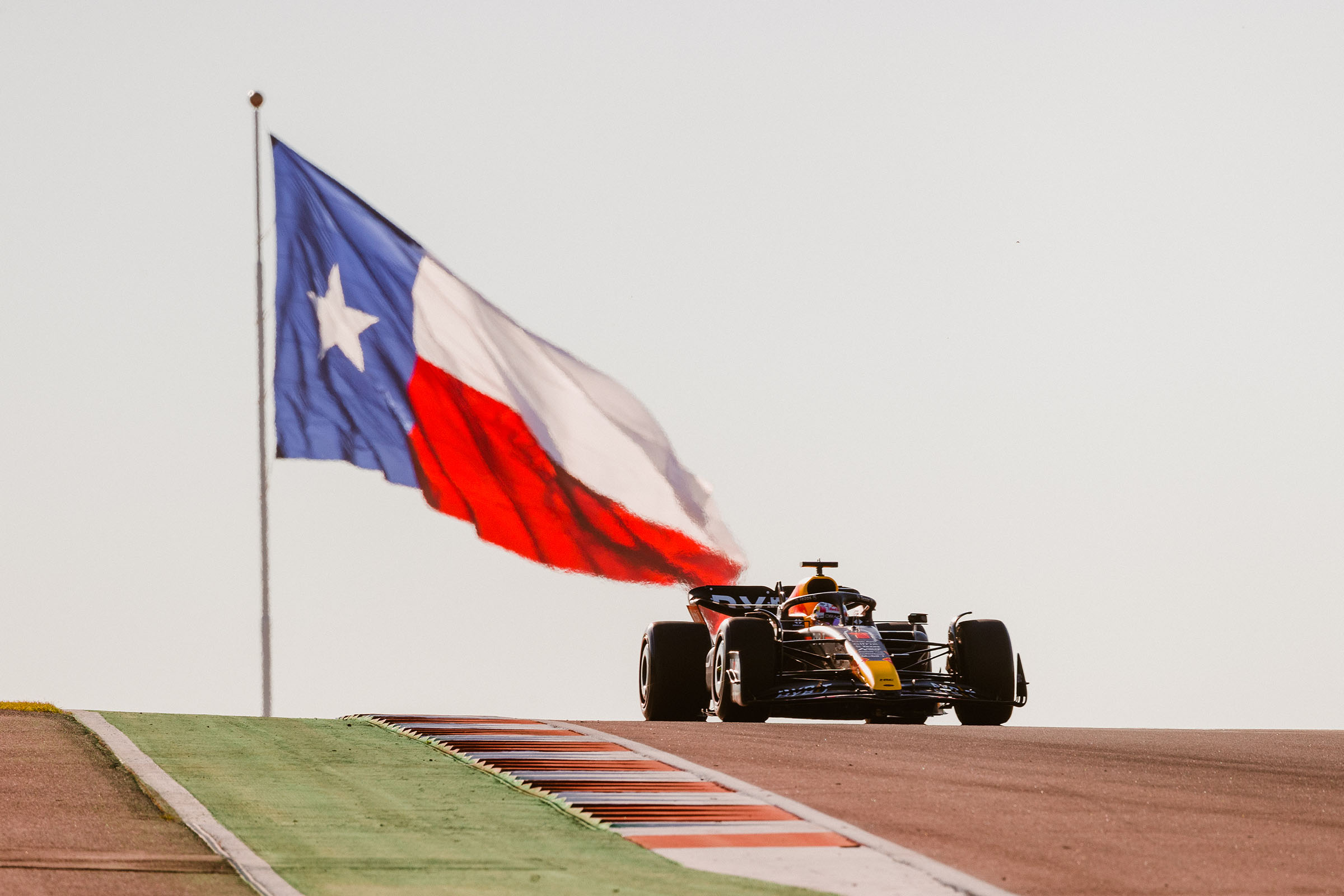 A Formula 1 car speeds down a track in front of a large Texas flag in the background