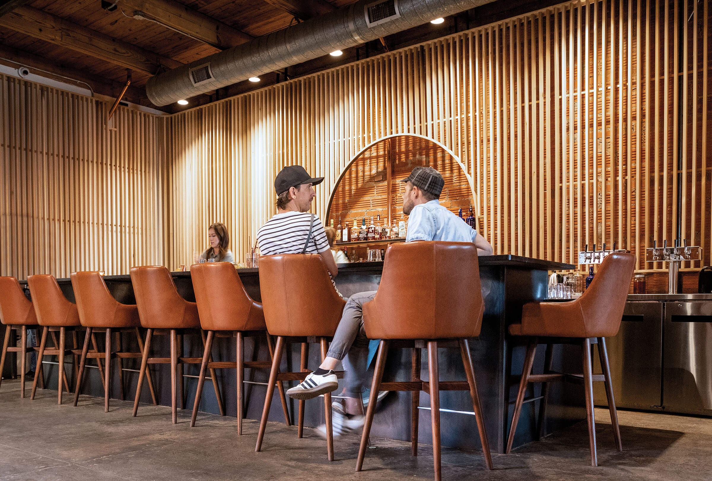 Two people sit in large leather barstools behind a wood-paneled bar