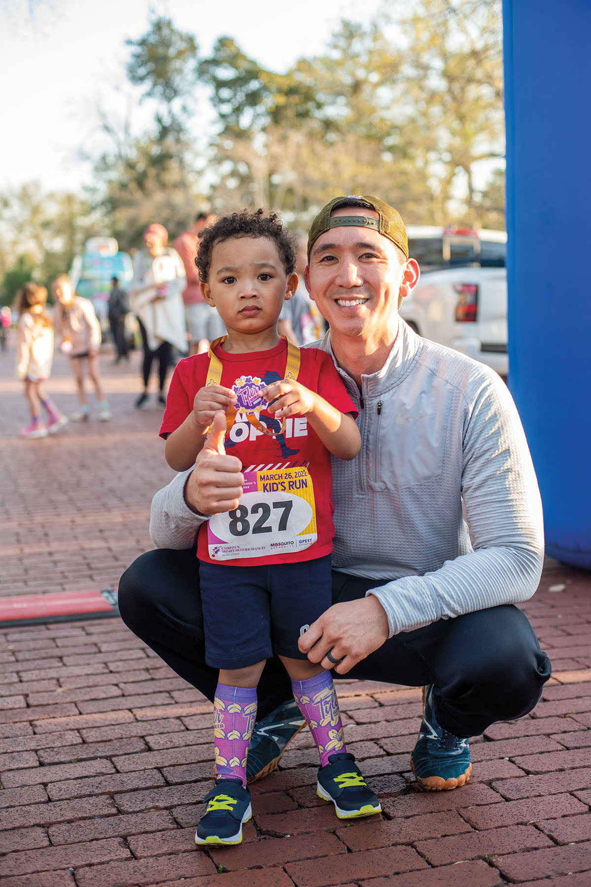 A man and child pose holding a race medal at a finish line