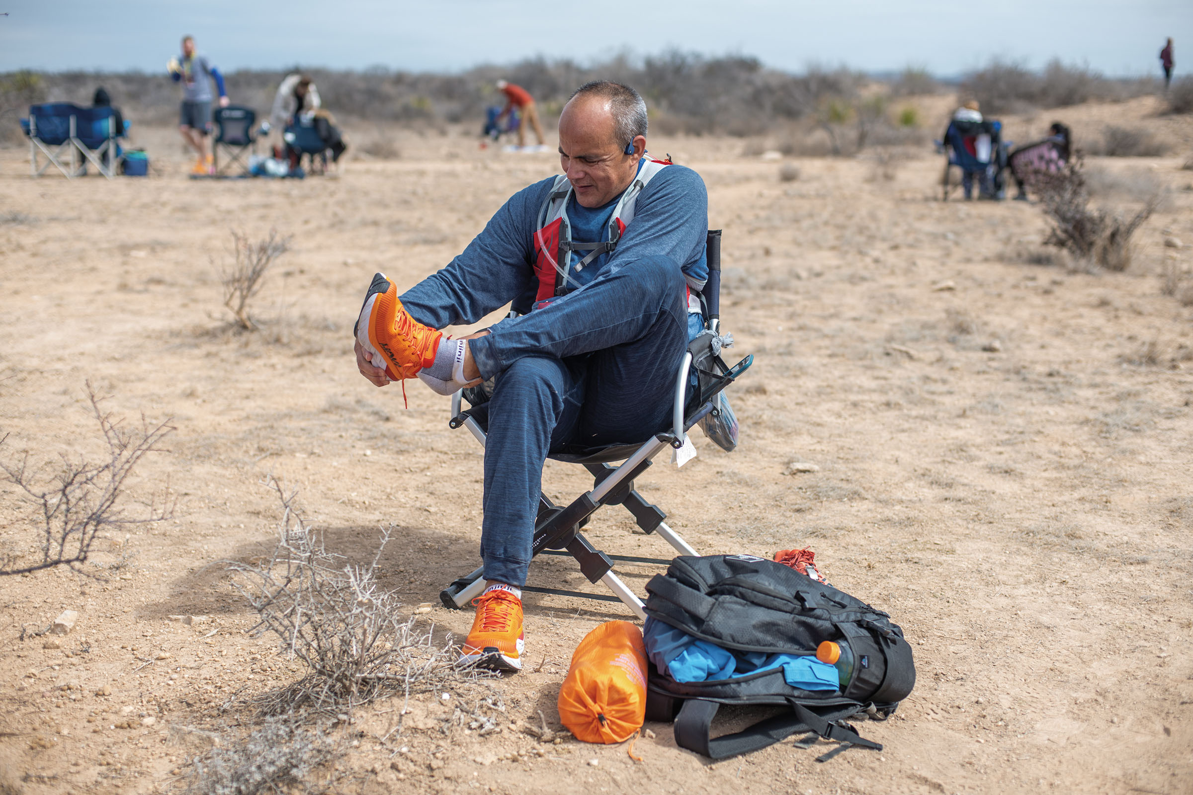 A man sits in a camp chair in a desert landscape lacing his shoes