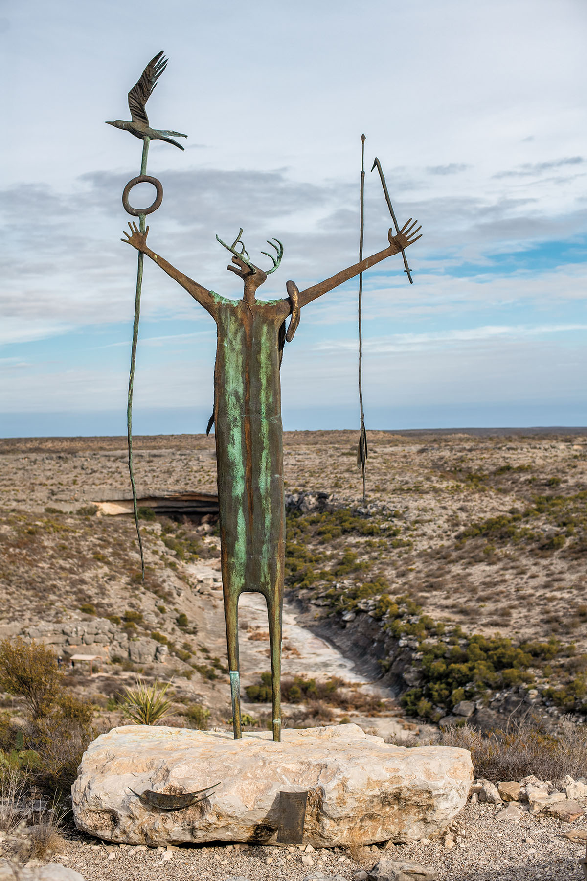 A statue of a figure with its arms outstretched on a desert landscape
