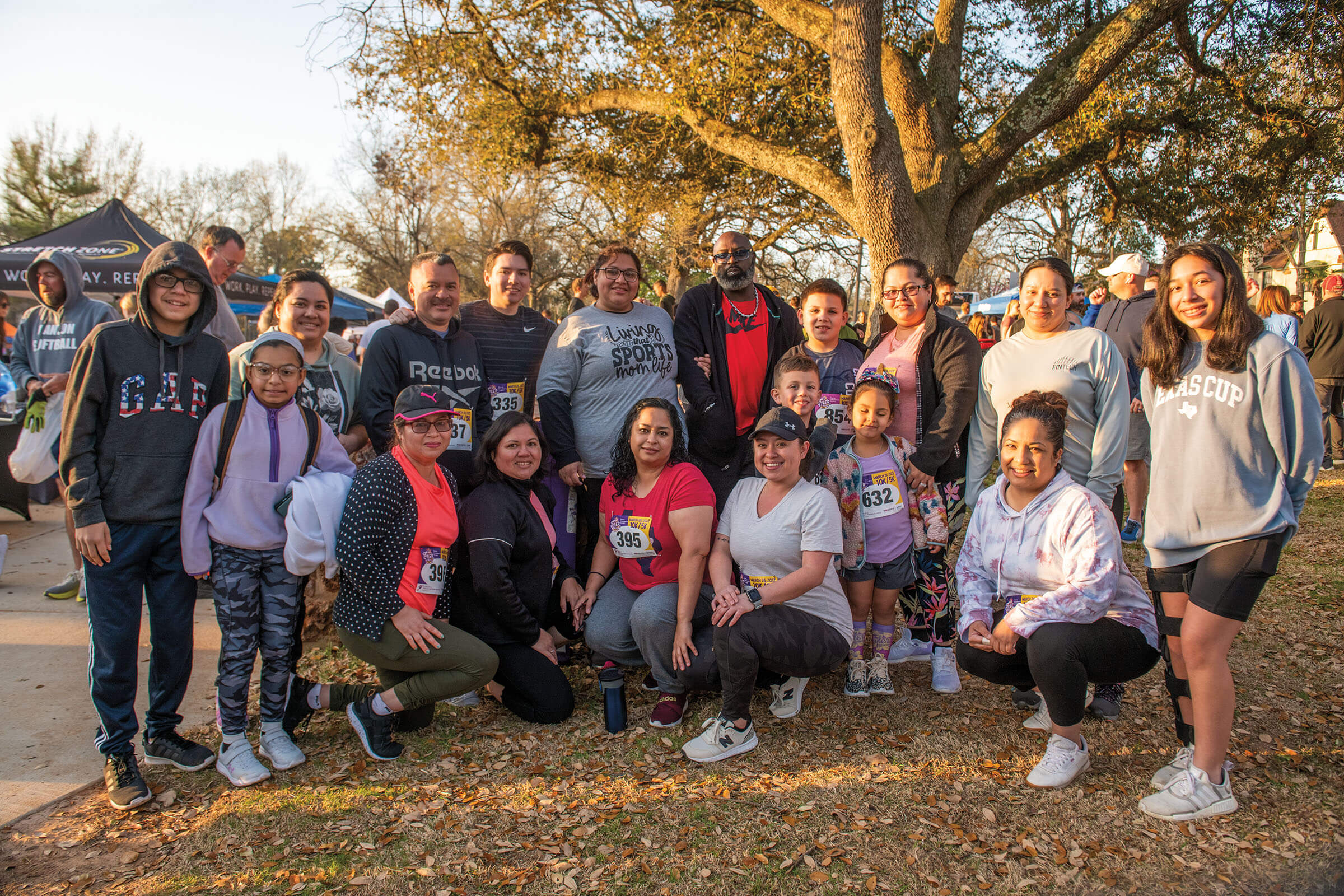 A group of people wearing racing attire stand in front of a large tree in golden light