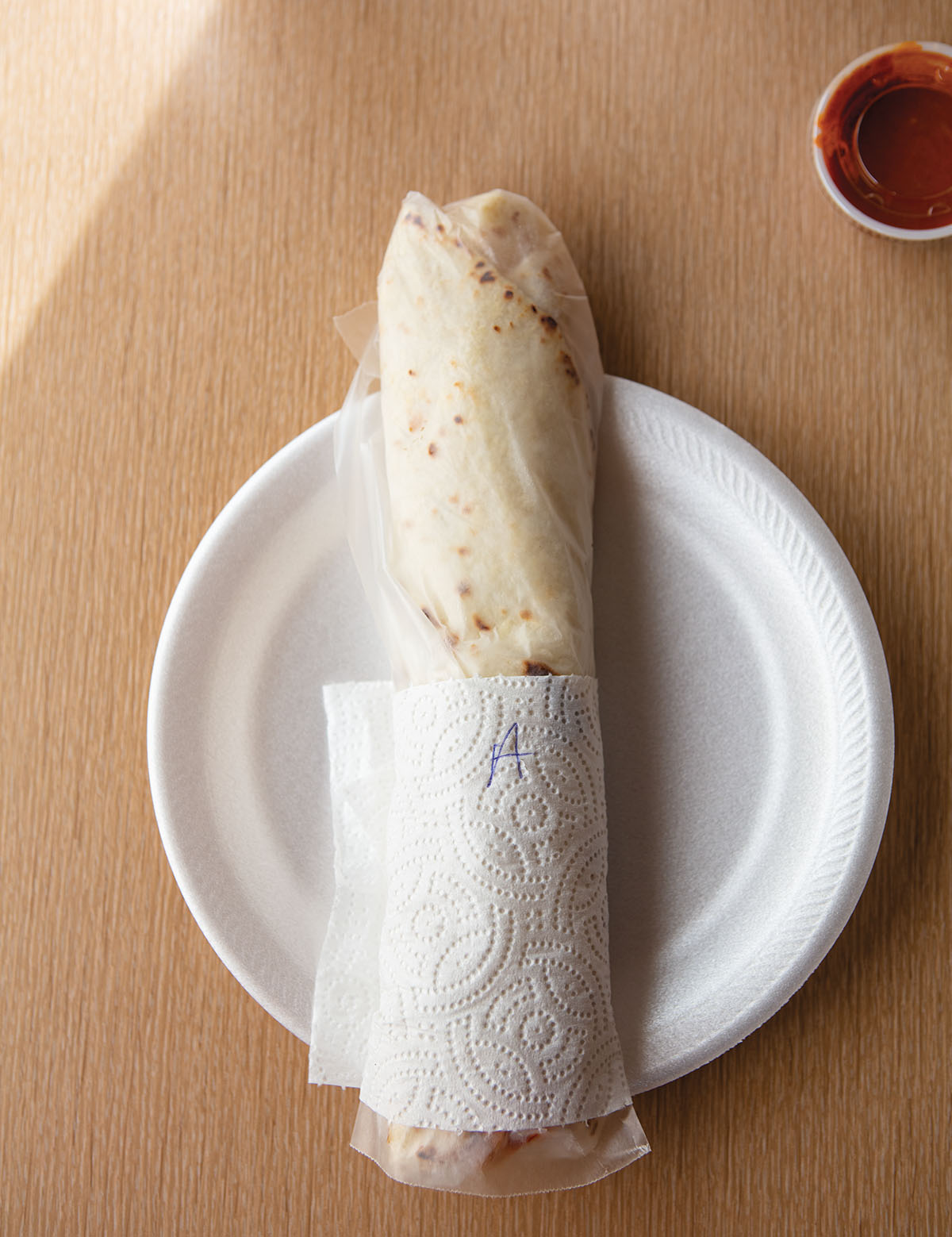 An overhead view of a burrito wrapped in a napkin sitting on a white paper plate