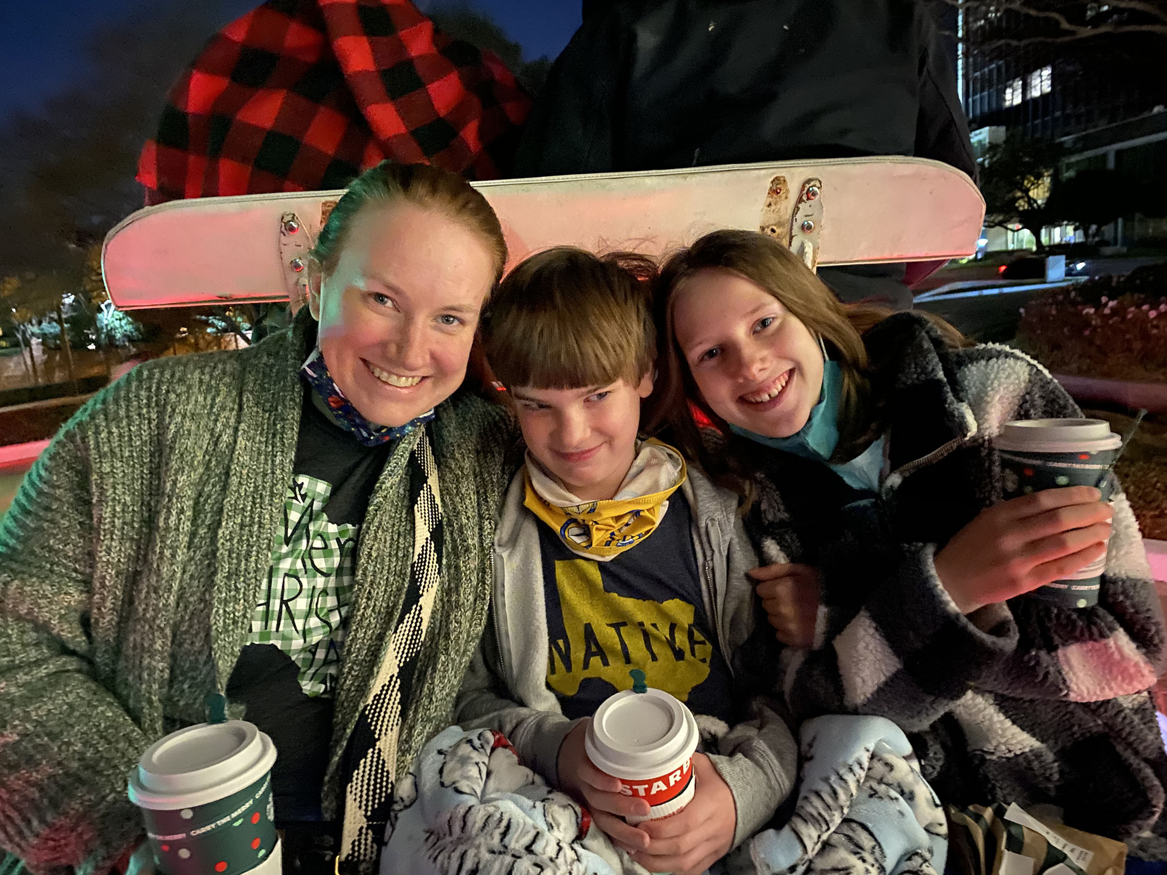 Katie Becker and her adolescent son and daughter sit in a carriage, cuddling up under a blanket and holding paper cups with hot chocolate. 
