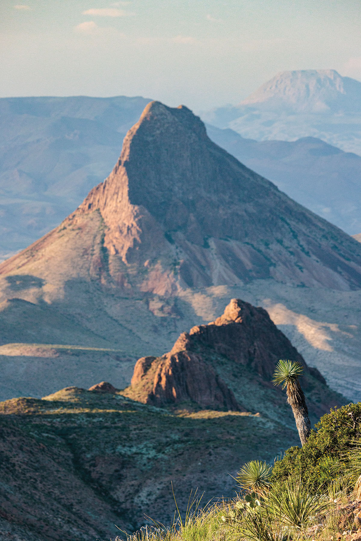 A tall mountain peak in front of other mountain peaks in an outdoor scene