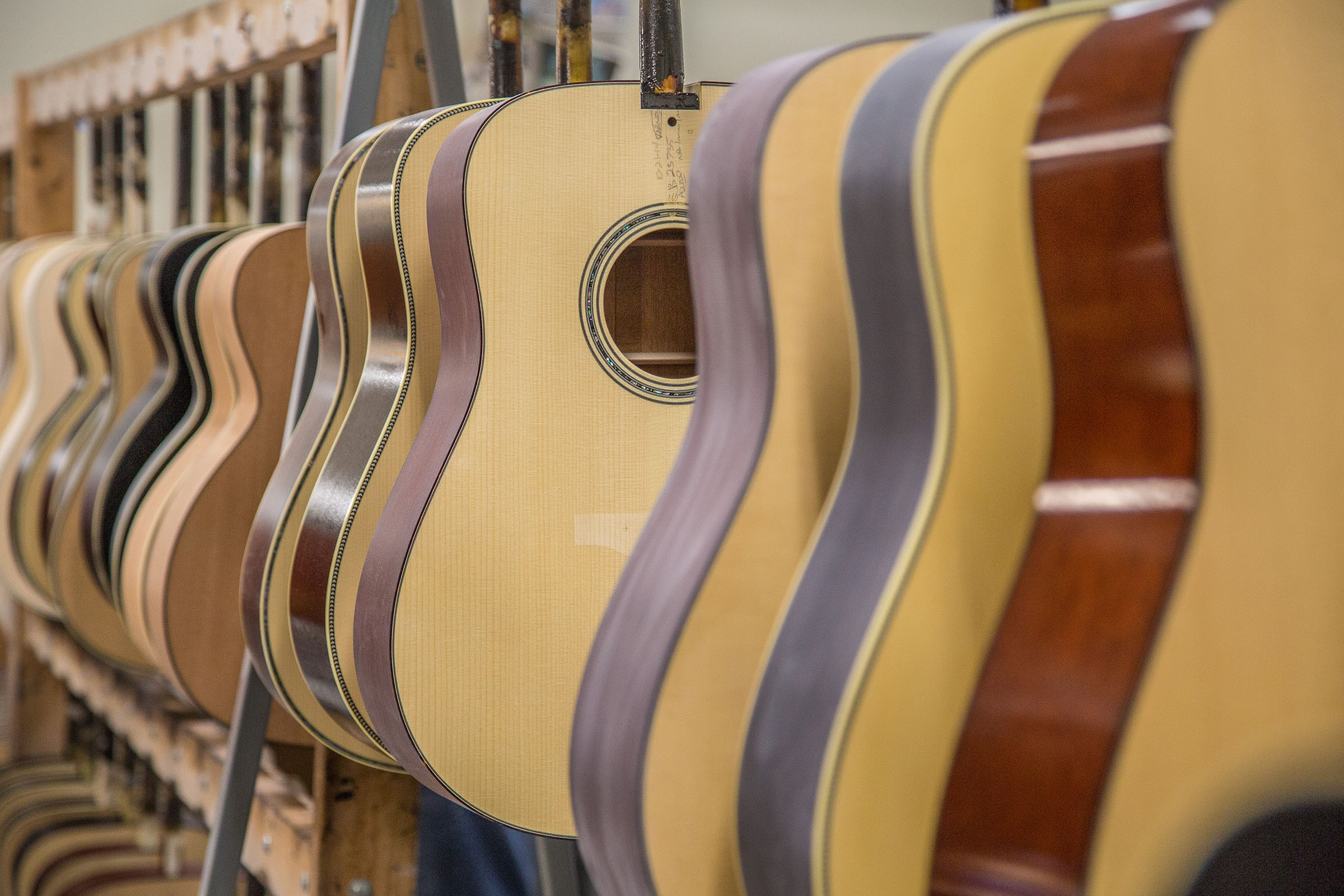 A collection of tan and brown guitars hang on a rack in a warehouse