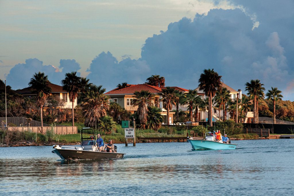 A collection of houses and palm trees line a waterway traveled by two boats