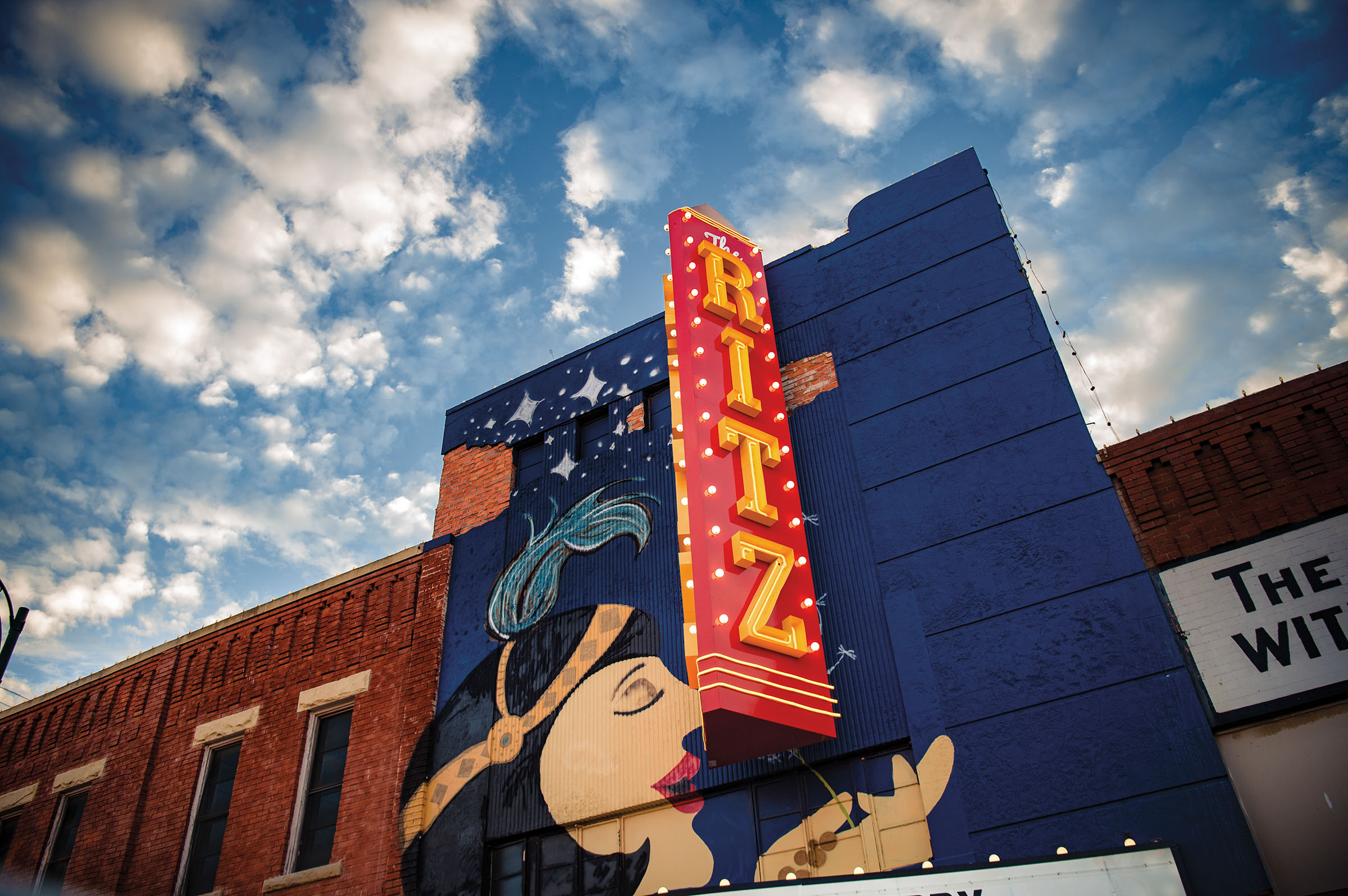 The exterior of a red and blue theater with a large sign reading "Ritz" under a blue sky with clouds