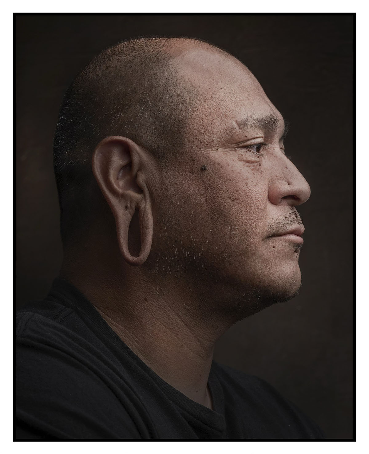 A side view of a man with stretched earlobes on a dark background