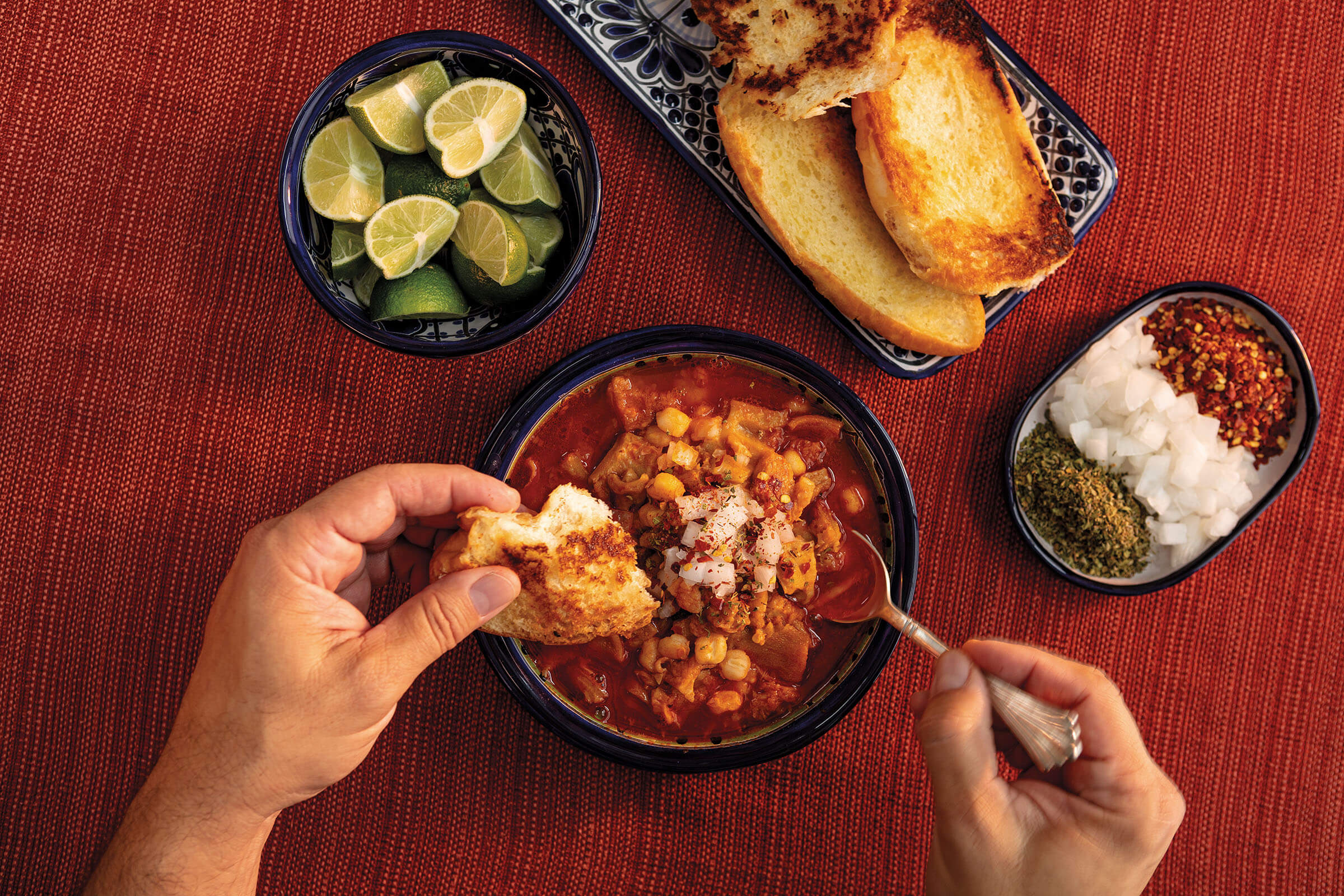 An overhead view of a rich red soup with various toppings served alongside