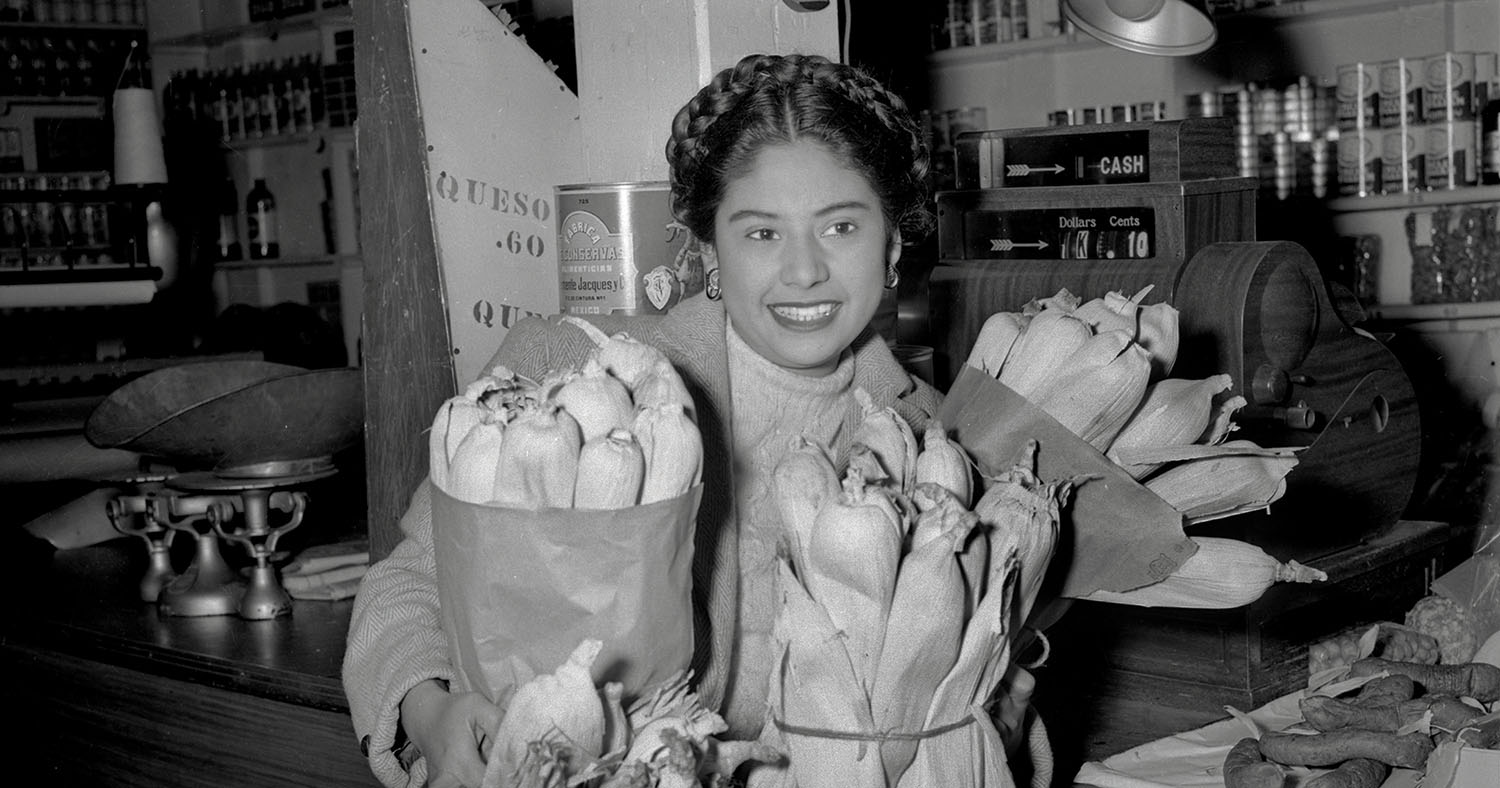 A black-and-white photograph of a woman holding tamales