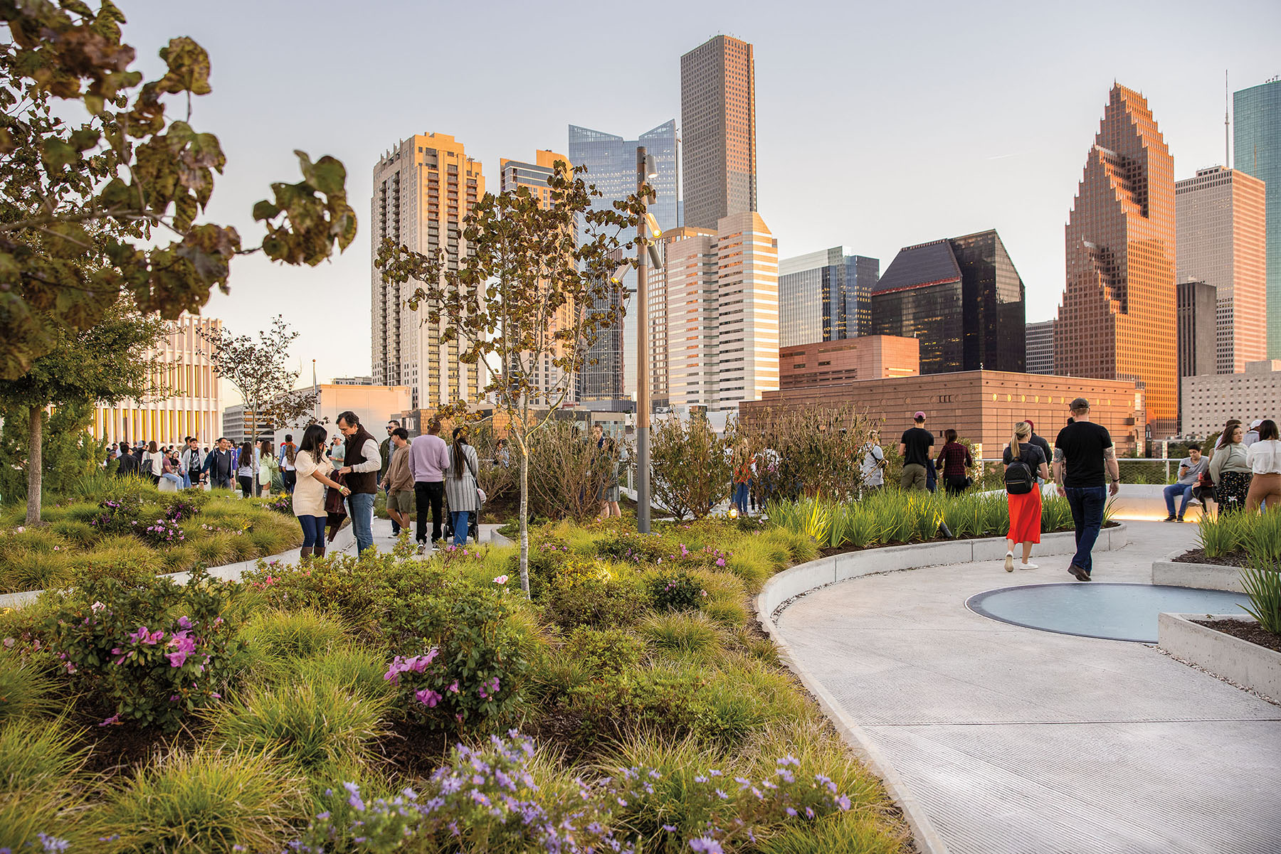 A grassy garden with a concrete pathway with the Houston downtown skyline in the background