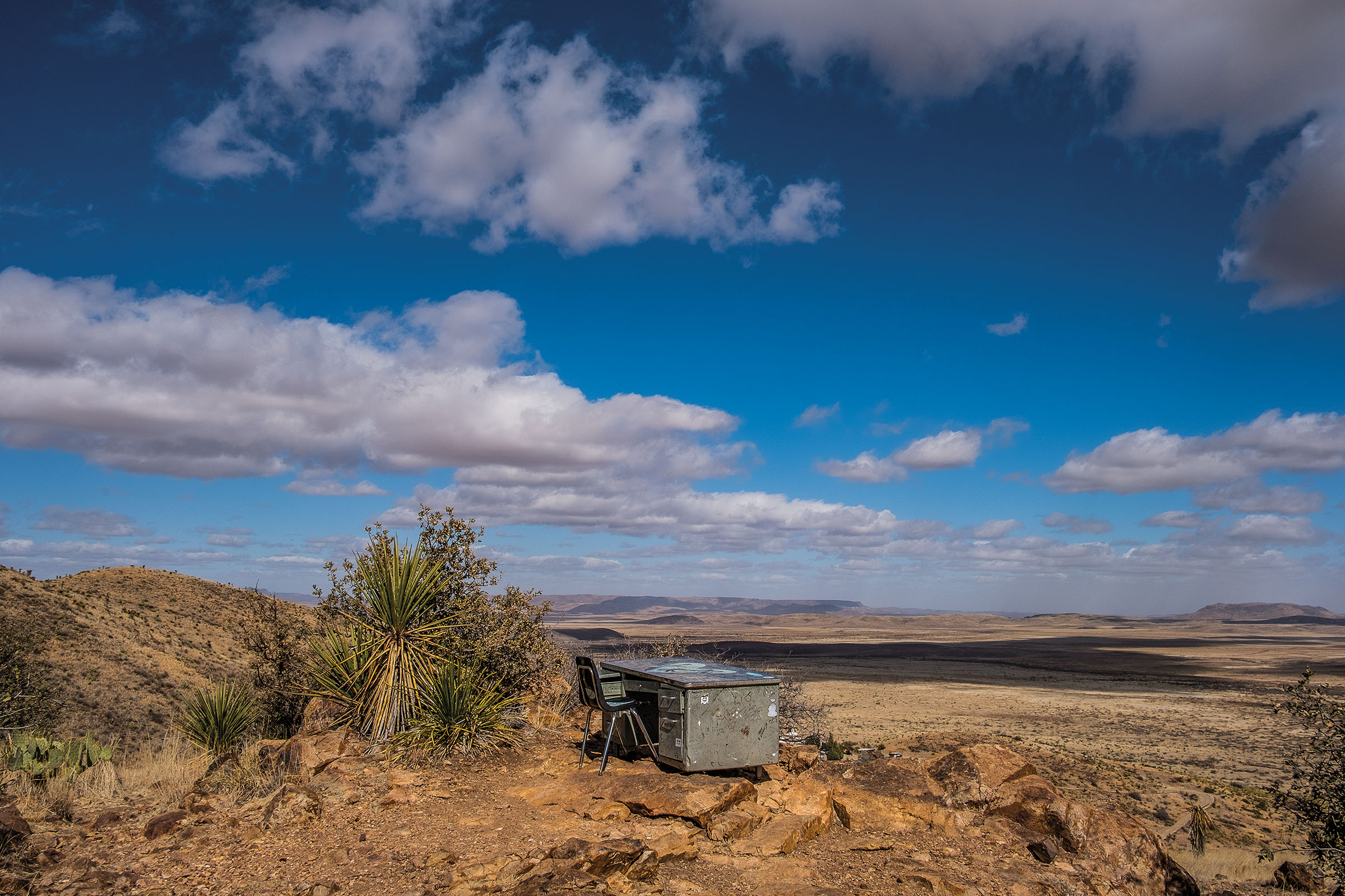 A school desk on top of a hill in a desert scene under blue sky