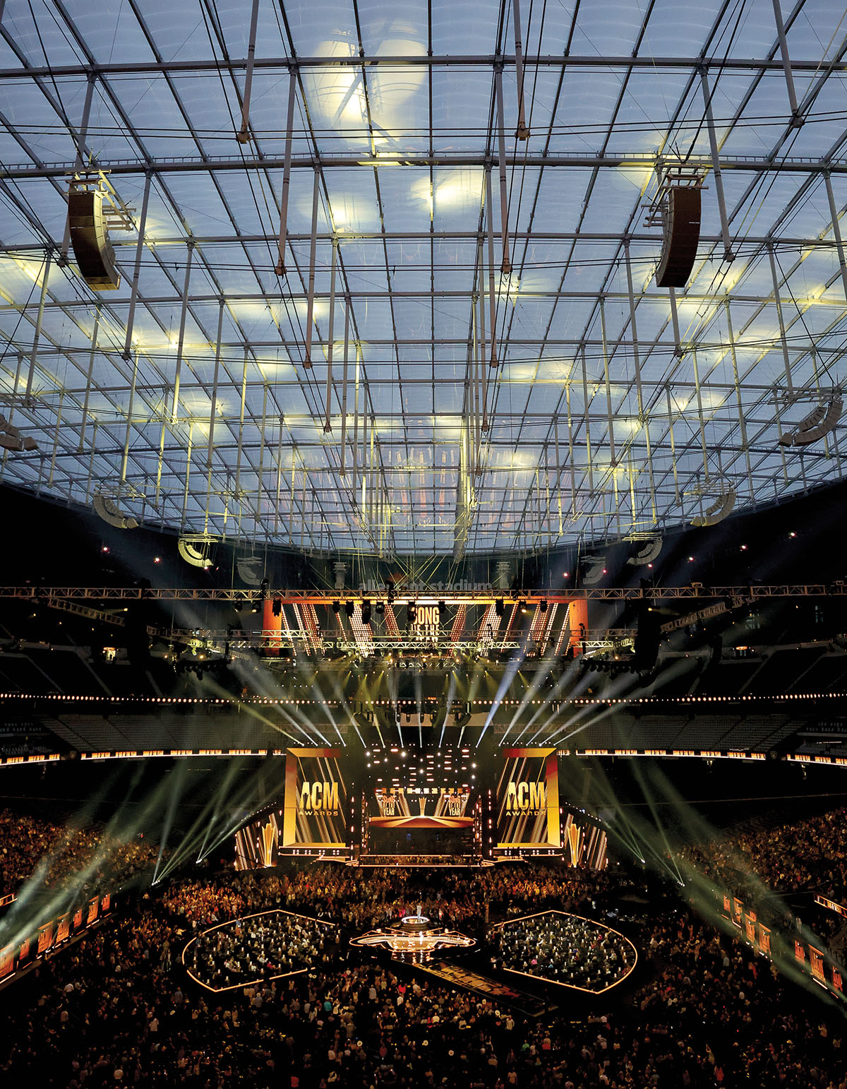 A photo of a large music venue during sunset with overhead speakers