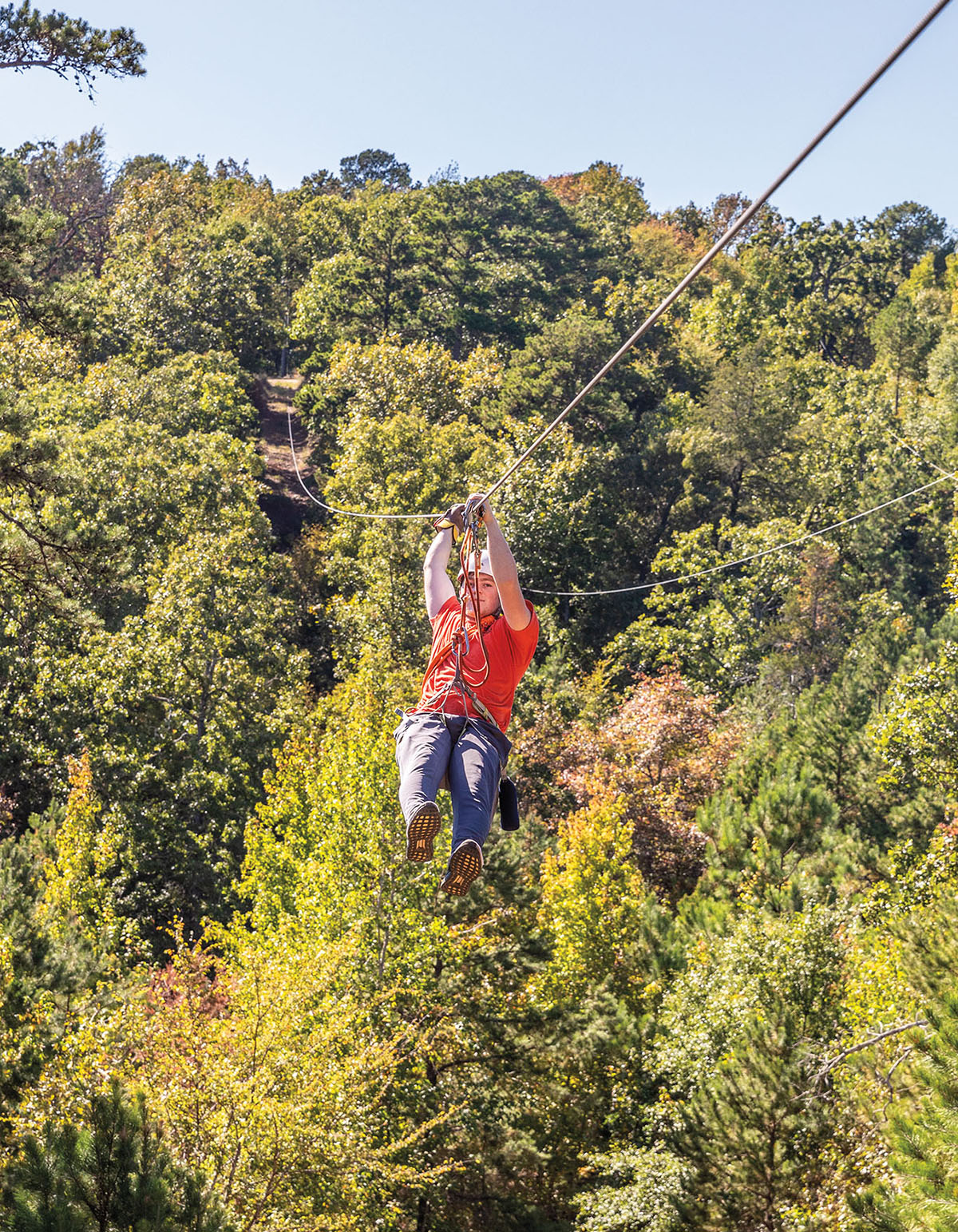 A person in a brightly colored shirt zip lines through green trees