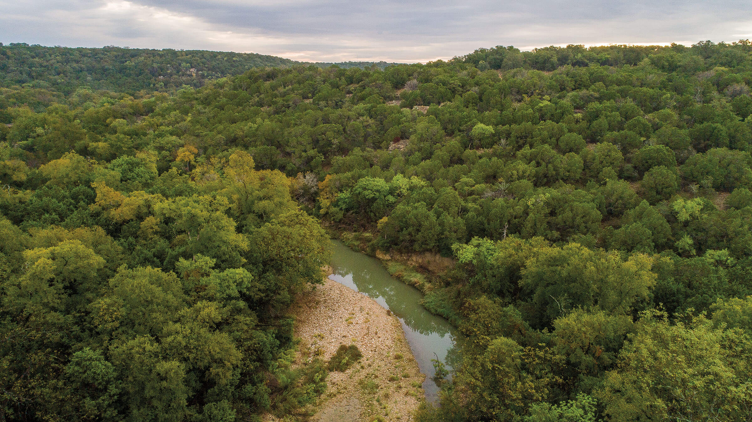 An overhead view of a small strip of water running through a large area of green trees